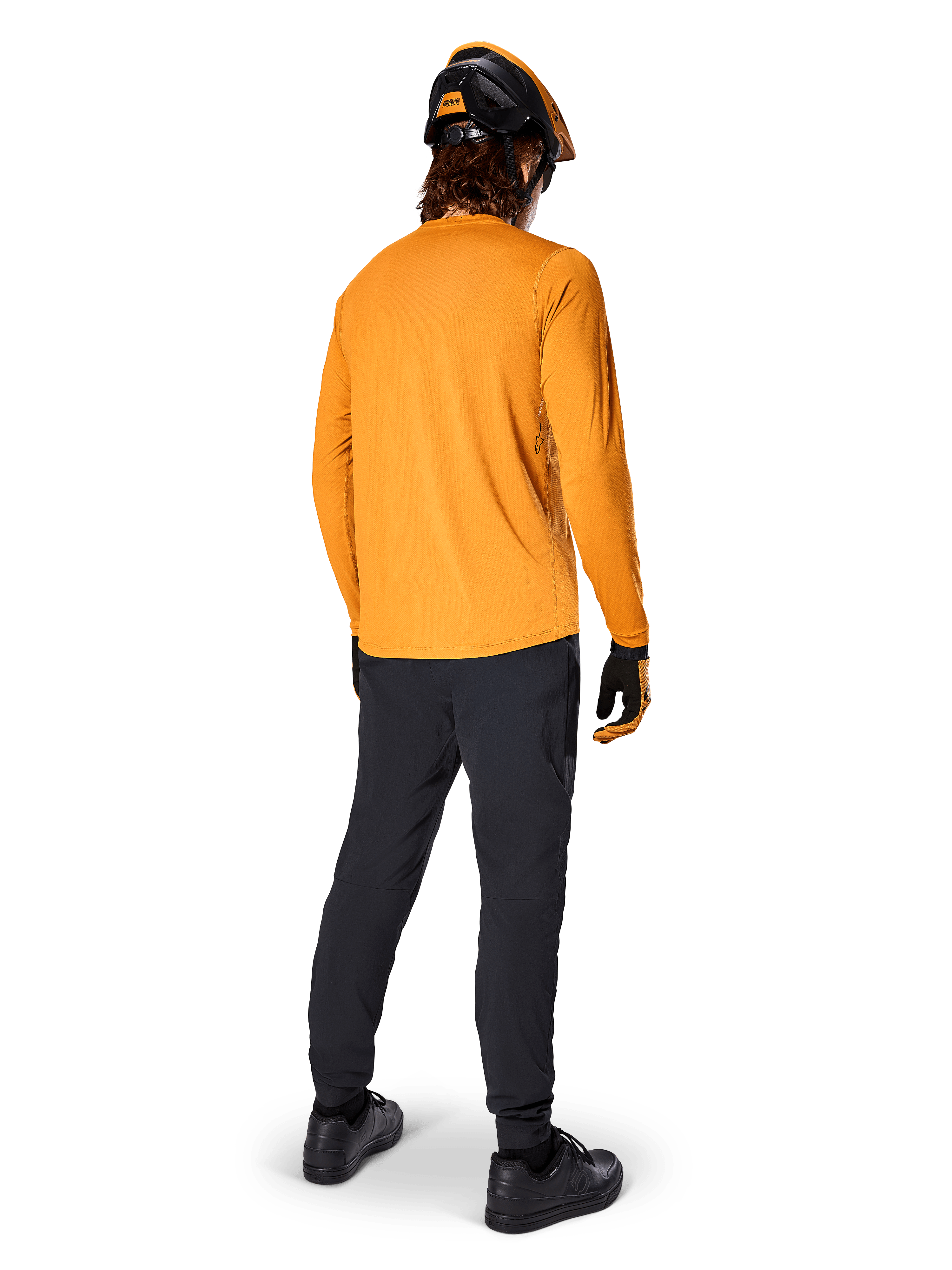 Ciclista de BTT visto de costas a usar a Camisola de Manga Comprida Alpinestars A-Dura Rocker em Dark Gold, calças pretas, capacete laranja e preto e sapatos pretos, equipamento técnico de BTT para trilhos