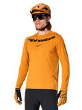 Camisola de manga comprida Alpinestars A-Dura Rocker, camisola de BTT, Dark Gold, pessoa a usar a camisola com capacete e luvas a condizer, visual desportivo coordenado com logótipo Alpinestars no peito