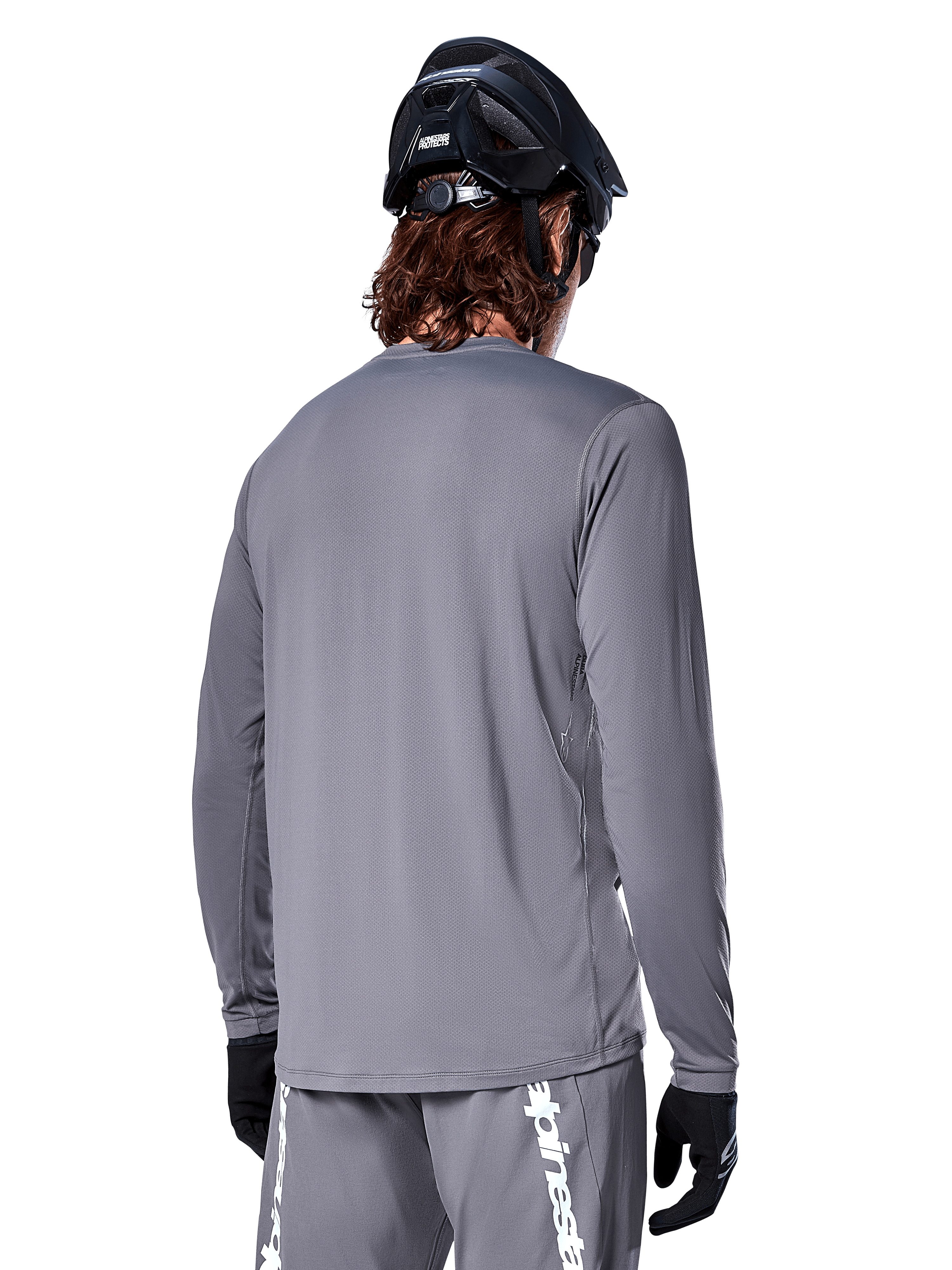 Alpinestars A-Dura Rocker Long Sleeve Jersey in Dark Gray, back view of mountain bike rider, paired with matching gray shorts featuring white branding, black MTB helmet, and black gloves, professional off-road cycling gear.