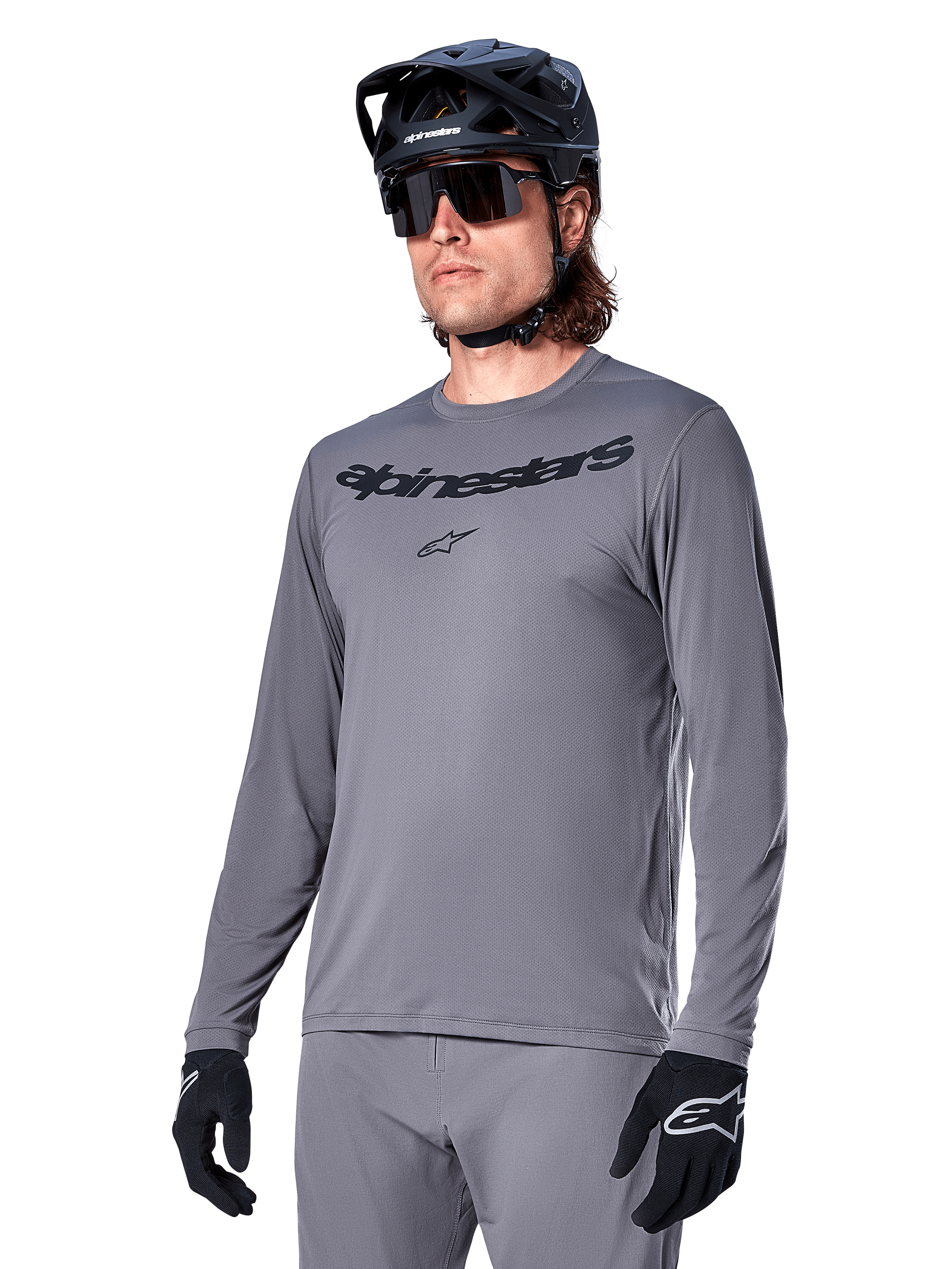 Camisola de manga comprida Alpinestars A-Dura Rocker, camisola de BTT cinzenta, usada com capacete e luvas pretas, com logótipo de texto preto no peito, vestuário de ciclismo desportivo para todo-o-terreno, fundo liso