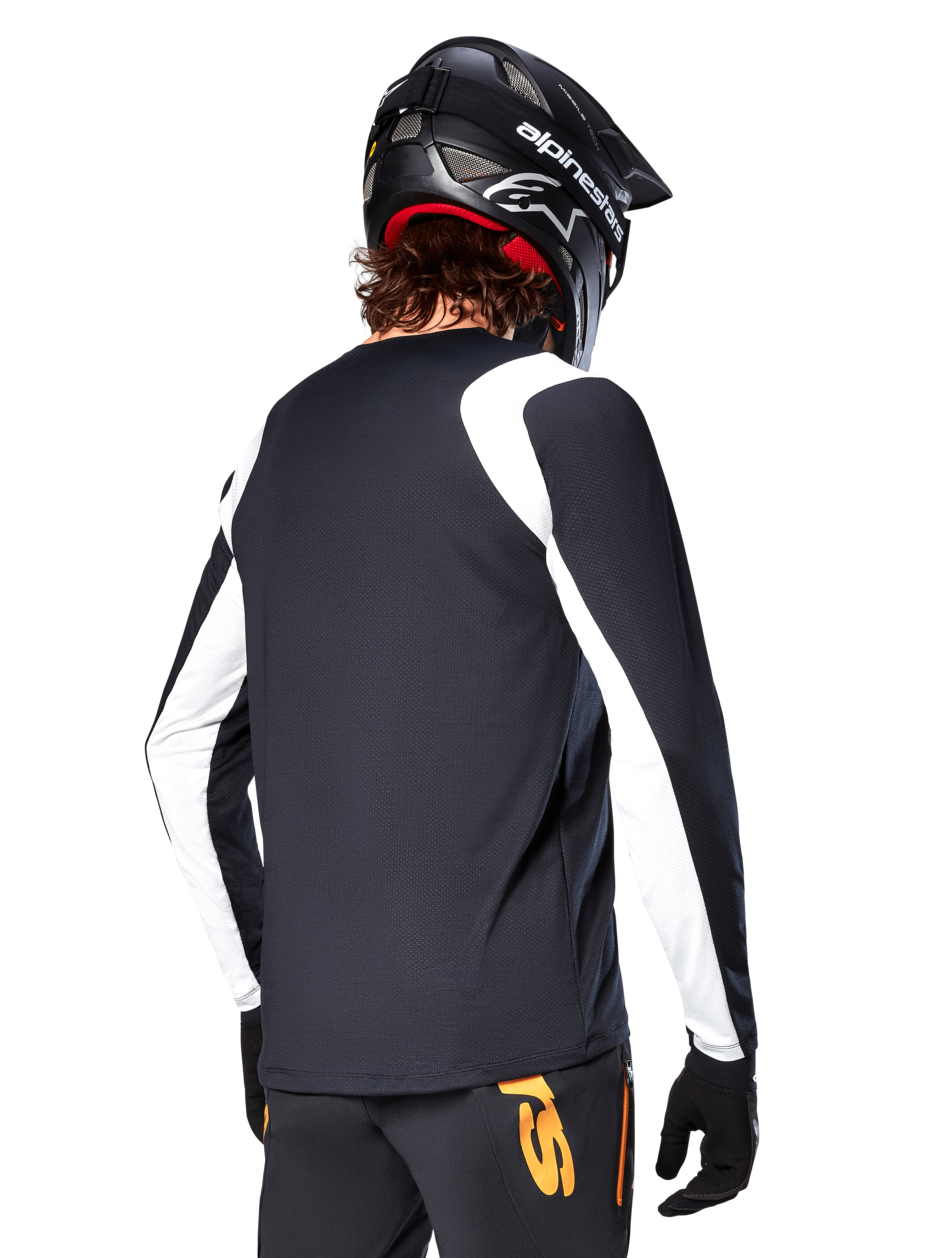 Ciclista de BTT a usar a Camisola de Manga Longa Alpinestars A-Supra Oscar, preta com painéis brancos nos ombros e mangas, vista de costas, capacete e luvas pretas, calças com detalhes laranja, equipamento de ciclismo de montanha durável
