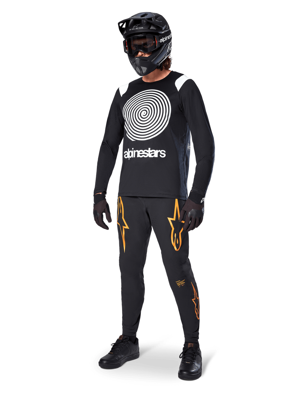 Ciclista de MTB com camisola de manga comprida Alpinestars A-Supra Oscar em preto, com grafismo espiral vintage Oscar em branco, calças pretas com logótipos de estrela em cor de laranja, capacete integral preto com óculos e luvas pretas, equipamento profissional de BTT