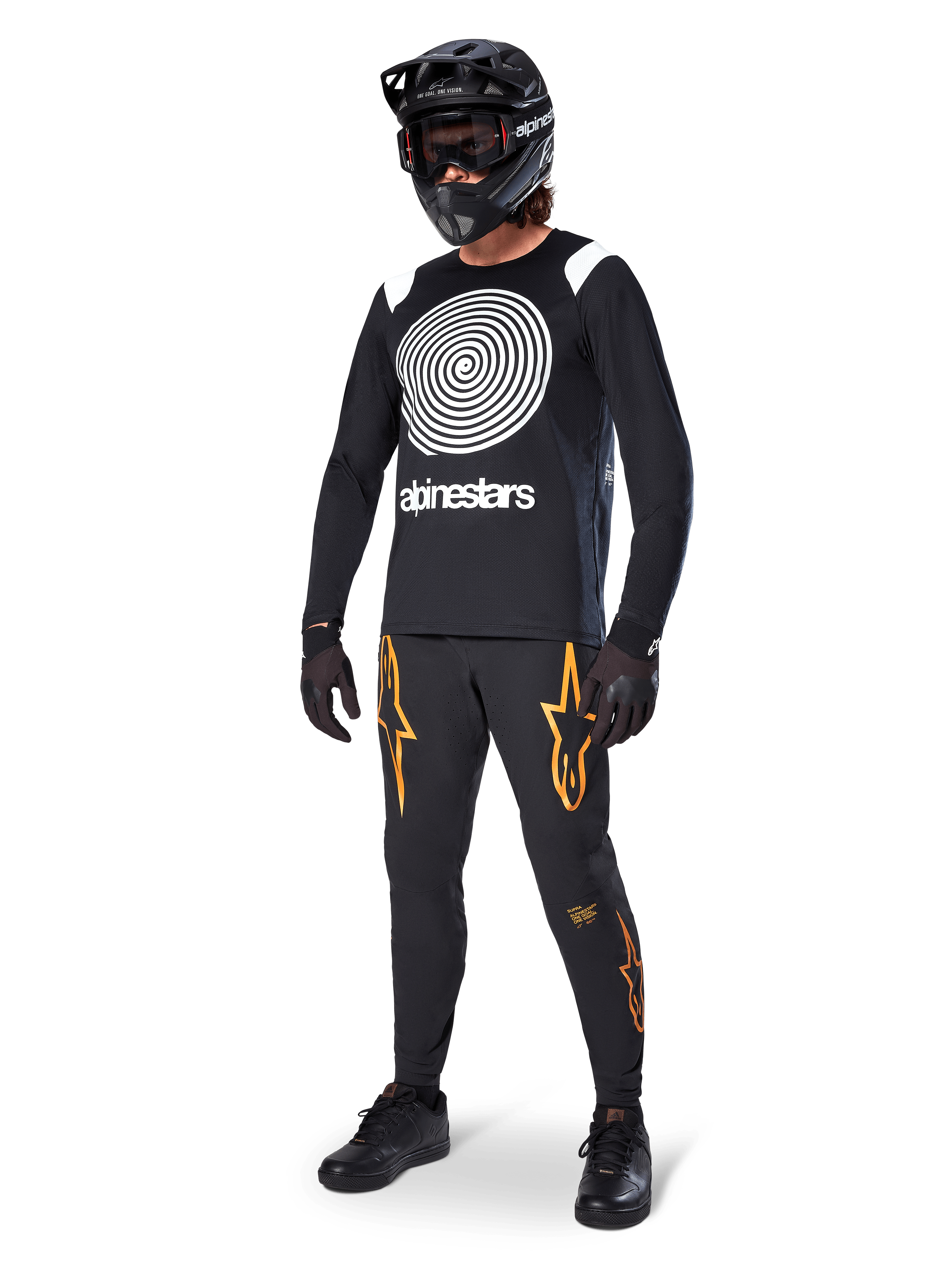 Ciclista de MTB com camisola de manga comprida Alpinestars A-Supra Oscar em preto, com grafismo espiral vintage Oscar em branco, calças pretas com logótipos de estrela em cor de laranja, capacete integral preto com óculos e luvas pretas, equipamento profissional de BTT