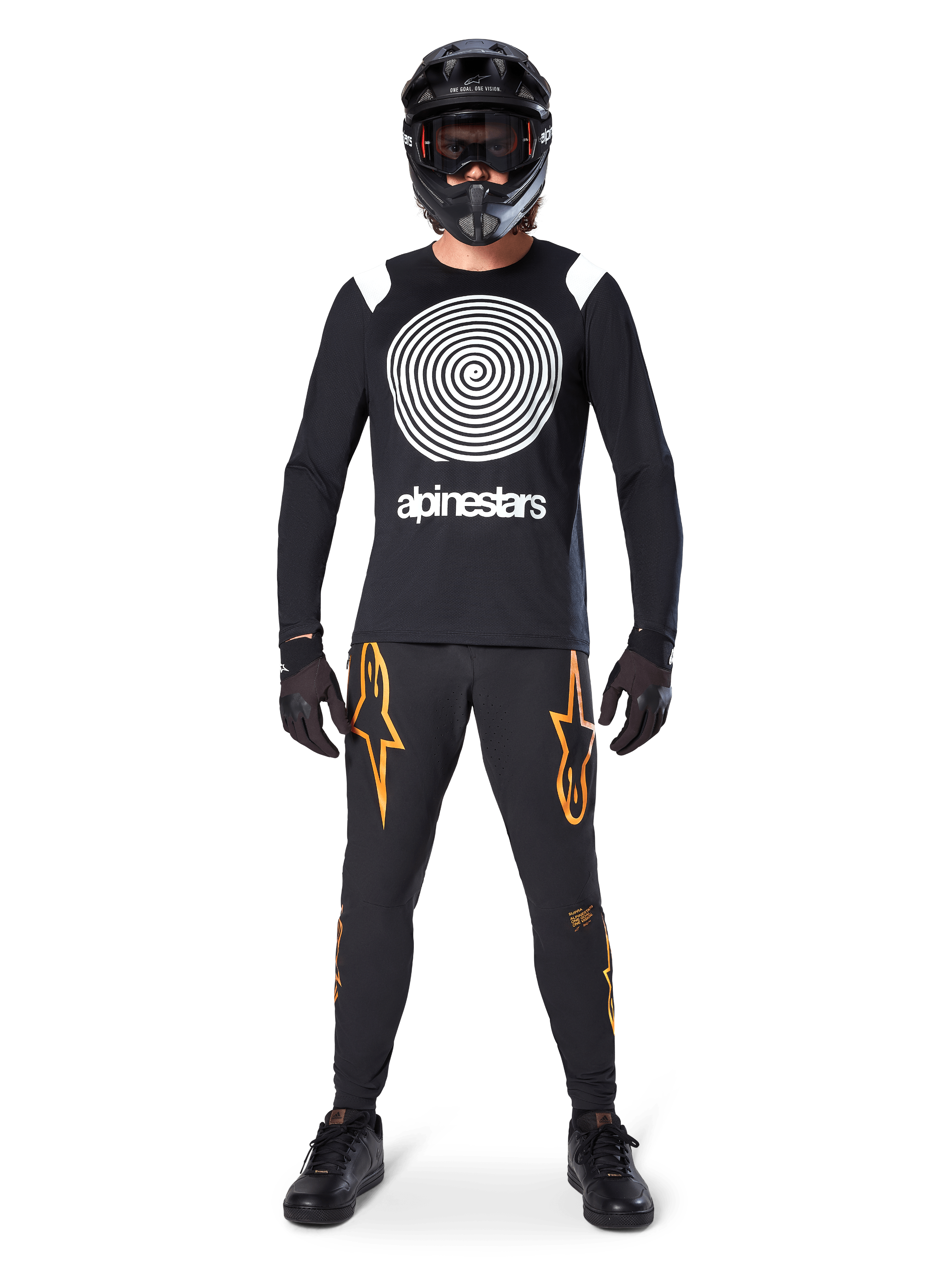 Modelo masculino com equipamento completo de mountain bike, Camisola de Manga Comprida Alpinestars A-Supra Oscar em preto com gráfico espiral branco no peito, calças pretas com logótipos de estrela cor de laranja, capacete integral e óculos pretos, luvas e sapatos pretos, conjunto coordenado para a prática de MTB gravity