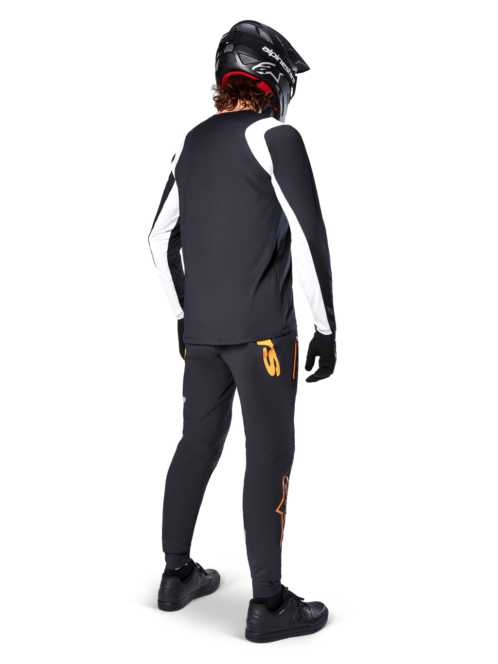 Camisola Alpinestars A-Supra Oscar de Manga Longa, preta com painéis brancos nas mangas, usada por um ciclista de MTB visto de costas, com capacete integral preto e calças pretas com logótipos cor de laranja, vestuário de ciclismo para gravidade off-road