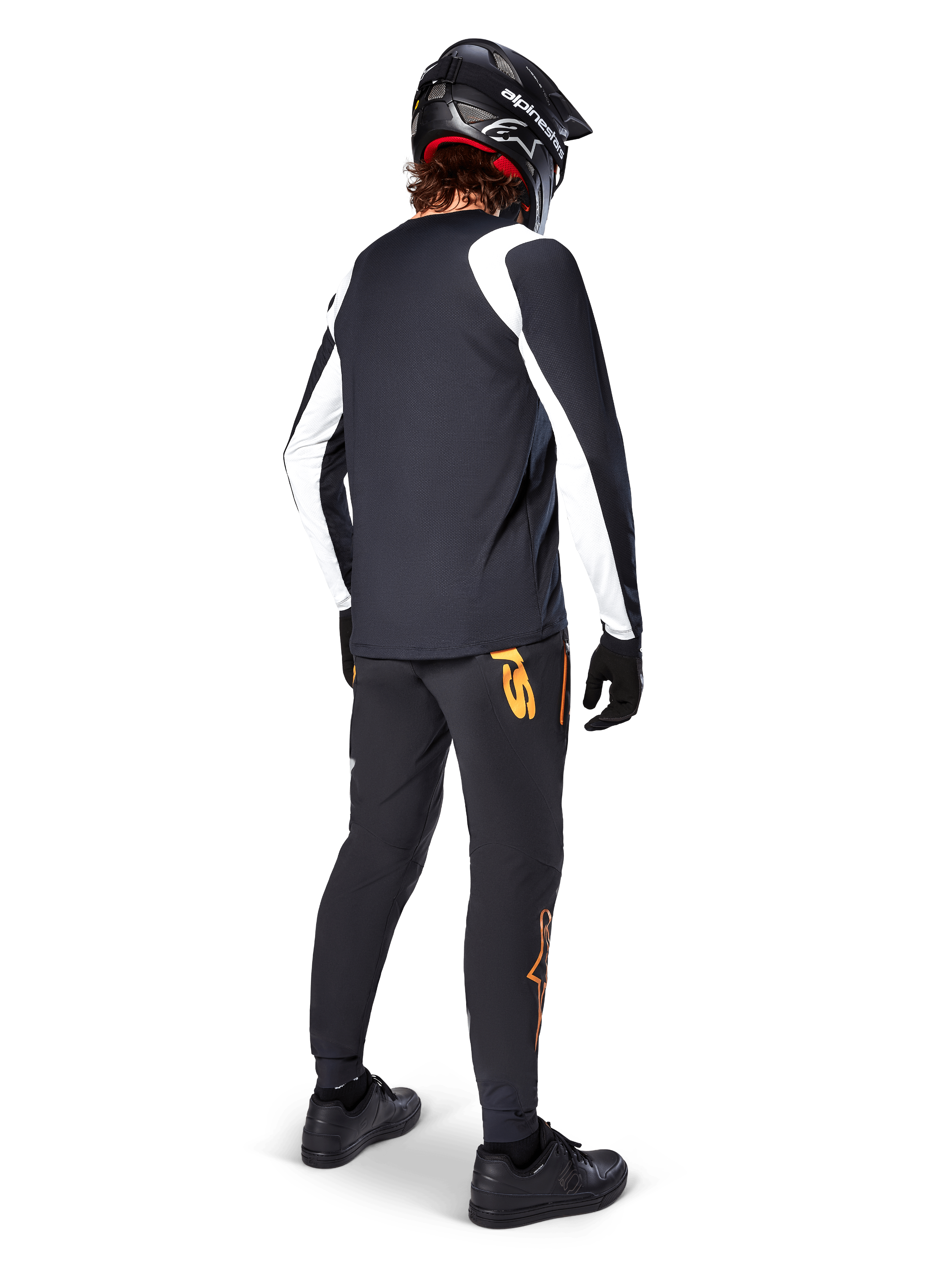 Camisola Alpinestars A-Supra Oscar de Manga Longa, preta com painéis brancos nas mangas, usada por um ciclista de MTB visto de costas, com capacete integral preto e calças pretas com logótipos cor de laranja, vestuário de ciclismo para gravidade off-road