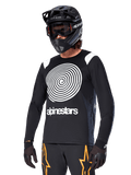 Alpinestars A-Supra Oscar Jersey de Manga Comprida, jersey de ciclismo MTB, preto e branco, com um design de espiral branca arrojado e logótipo Alpinestars no peito, usada com capacete integral preto e óculos de proteção, vestuário de performance para BTT