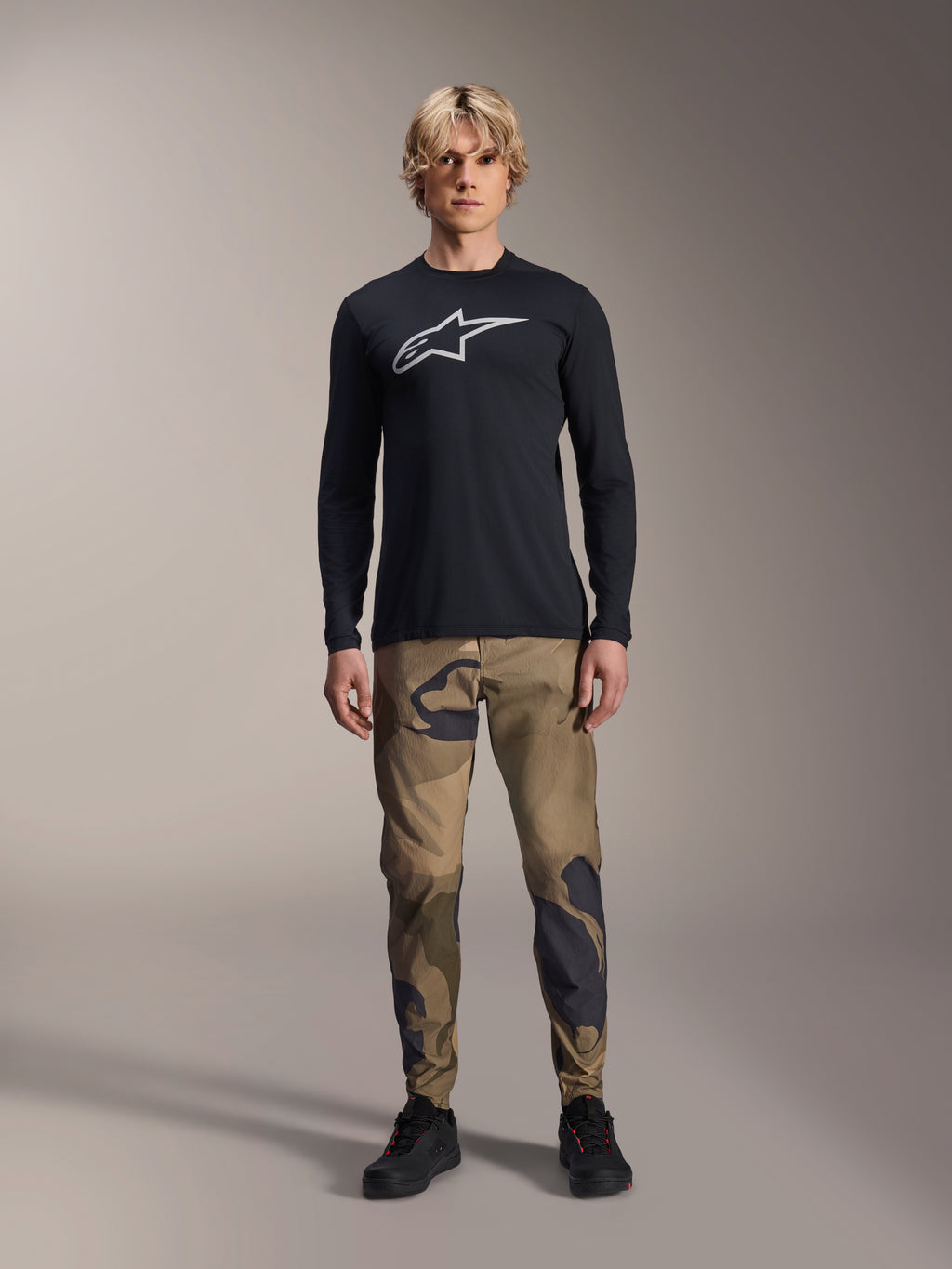Alpinestars A-Dura Camo Pant, MTB Cycling Pants, Brown and Green Camouflage, worn with a black long-sleeve jersey and black shoes, sporty mountain bike style with durable stretch fabric
