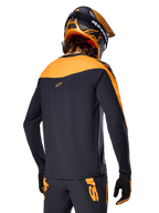 Alpinestars A-Supra Race Jersey - Manga Comprida, preto e laranja, vista traseira de ciclista com capacete e calças de BTT a condizer, ajuste de performance com textura microperfurada, equipamento de corrida profissional de BTT