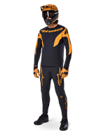 Ciclista de MTB com equipamento de corrida completo, Camisola A-Supra Race preta com detalhes laranja, calças pretas a condizer com logótipos Alpinestars laranja, capacete integral laranja e preto com óculos, luvas laranja e preto, conjunto coordenado para corridas de mountain bike
