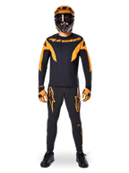 Ciclista de BTT com camisola Alpinestars A-Supra Race - Manga Comprida em preto e laranja, calças, luvas e capacete integral com óculos de proteção a condizer, kit de BTT coordenado para competição e performance fora de estrada