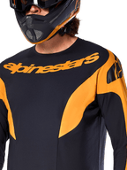 Alpinestars A-Supra Race Jersey - Manga Comprida, camisola de MTB, preta com painéis gráficos laranja, logótipo Alpinestars laranja no peito, exibida num piloto com capacete integral condizente em preto e laranja, vestuário de performance para corridas de MTB