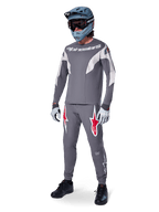 MTB rider wearing Alpinestars A-Supra Race Jersey, Long Sleeve, Dark Gray with light gray accents, matching dark gray pants featuring red star logo, gray full-face helmet with goggles, light gray gloves, coordinated outfit for mountain bike racing