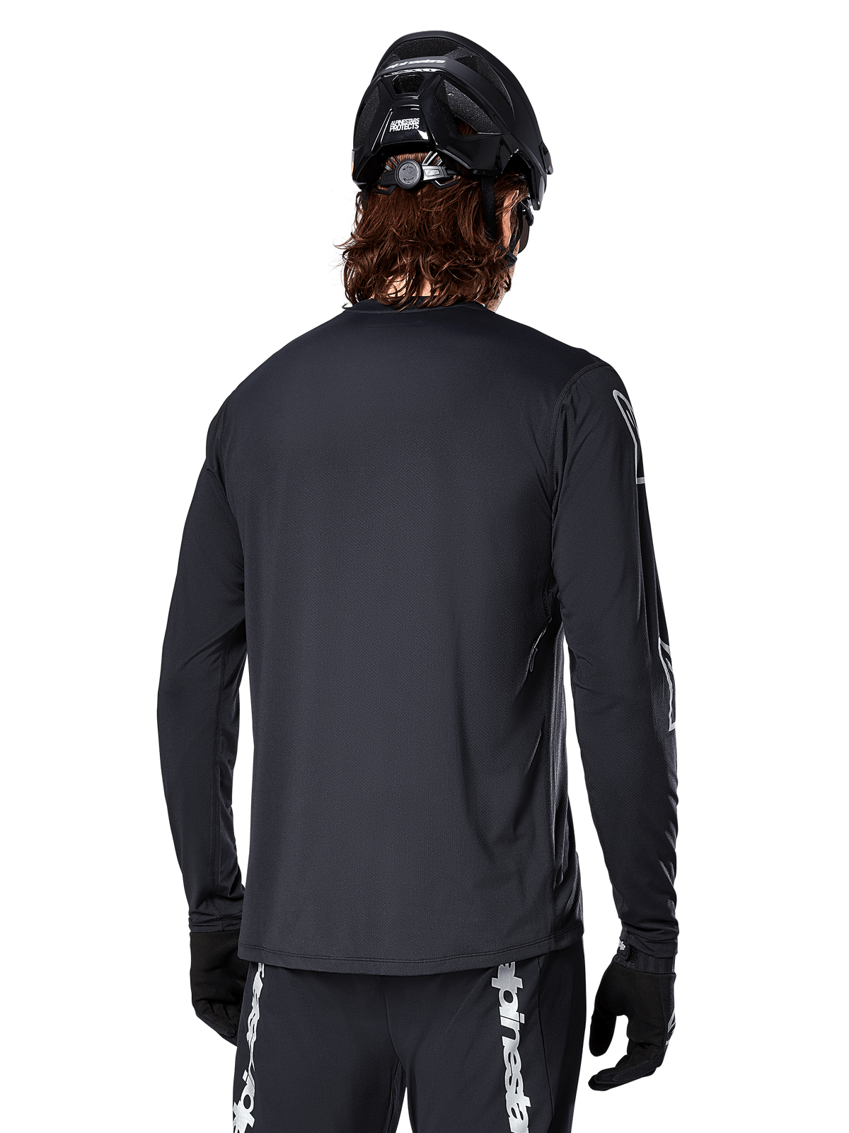 Alpinestars A-Dura Switch Long Sleeve Jersey, preto, vista traseira num ciclista a usar capacete de BTT e luvas pretas, com tecido jacquard técnico e parte traseira mais comprida para ciclismo fora de estrada