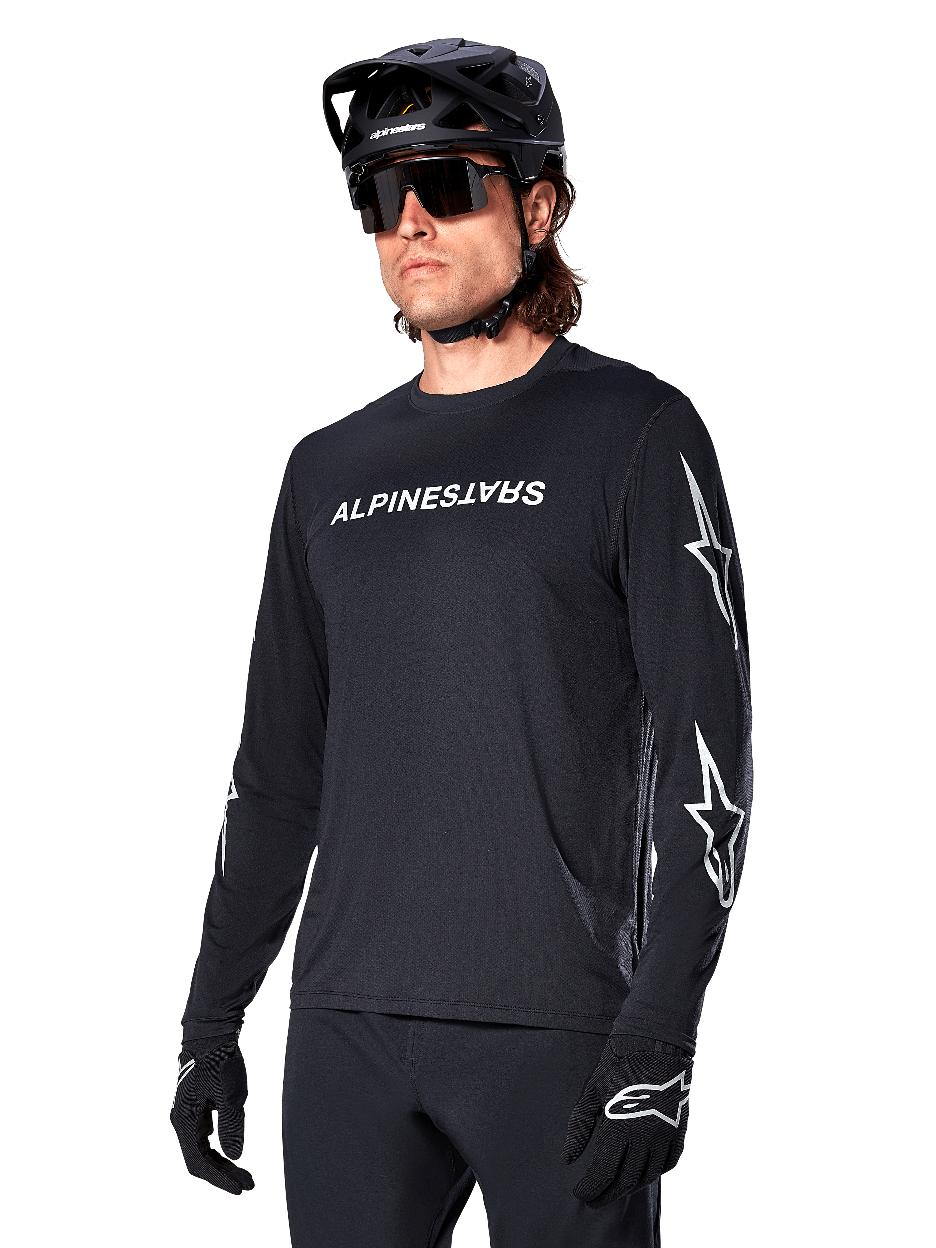Male cyclist wearing Alpinestars A-Dura Switch Long Sleeve Jersey, Black with white wordmark and star logos on sleeves, styled with black MTB helmet and sunglasses, high-performance cycling gear for off-road riding