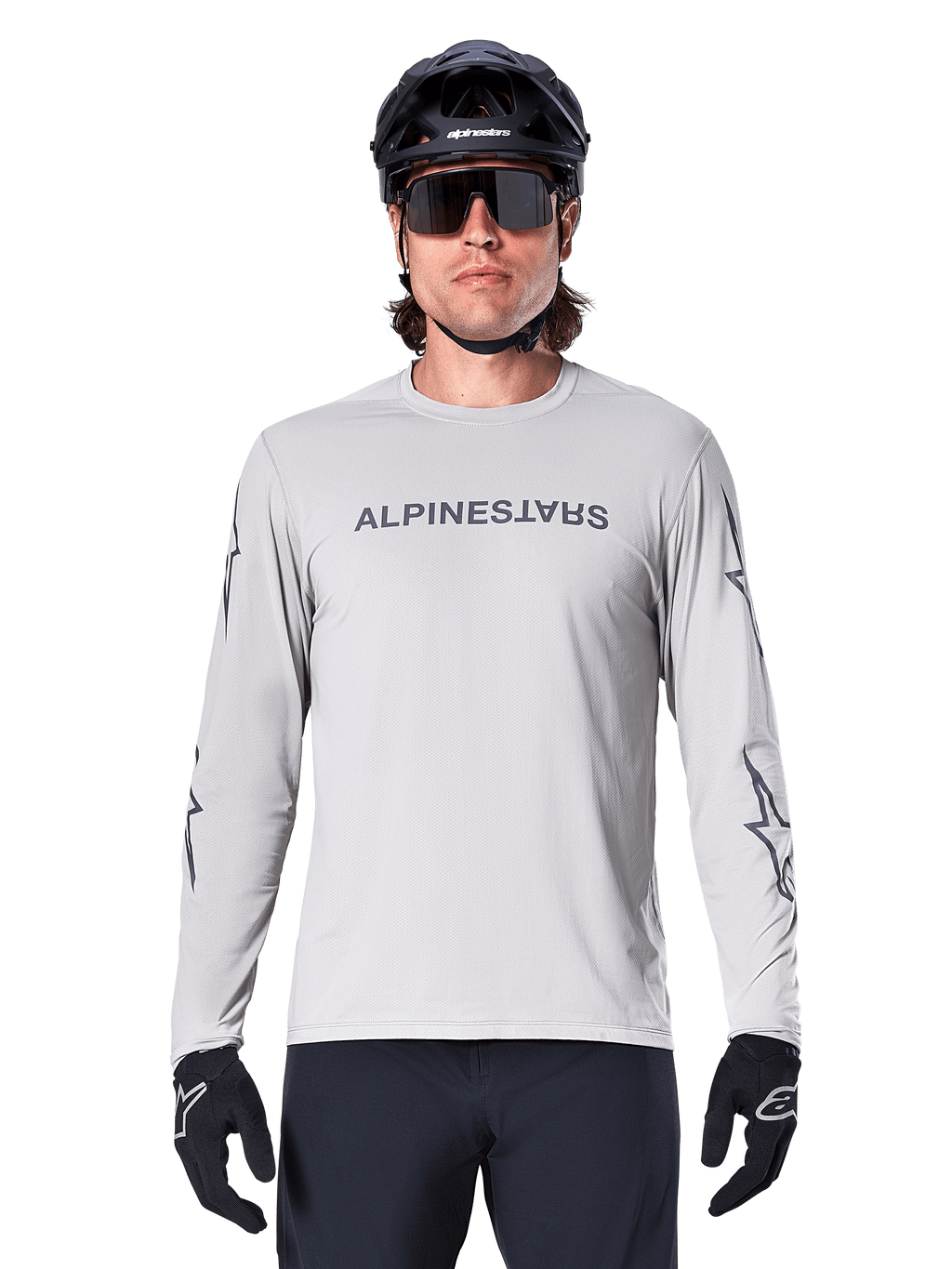 Camisola de Manga Comprida Alpinestars A-Dura Switch, Cinzento Claro, apresenta logótipo nominativo no peito e logótipos de estrela nas mangas em cinzento escuro, usada por um ciclista com capacete de BTT e luvas pretas, vestuário de ciclismo de performance para trilhos