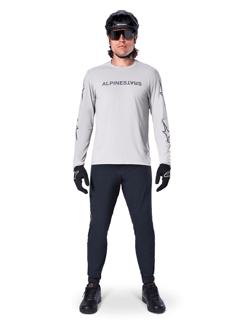 Camisola de Manga Comprida Alpinestars A-Dura Switch em Cinzento Claro, com logótipo estilizado no peito, usada com calças pretas, capacete e luvas, vestuário de performance para BTT e ciclismo fora de estrada
