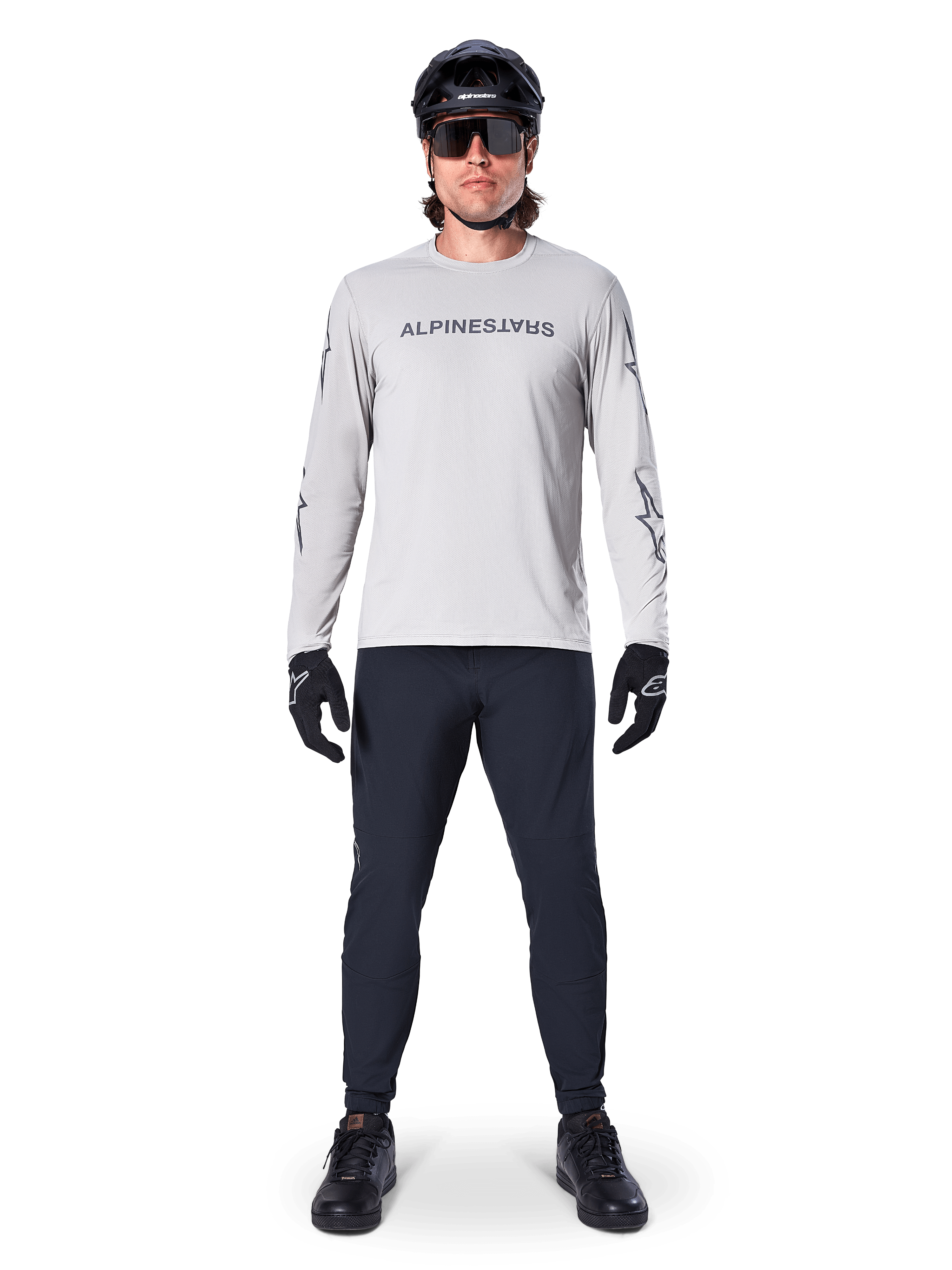 Camisola de Manga Comprida Alpinestars A-Dura Switch em Cinzento Claro, com logótipo estilizado no peito, usada com calças pretas, capacete e luvas, vestuário de performance para BTT e ciclismo fora de estrada