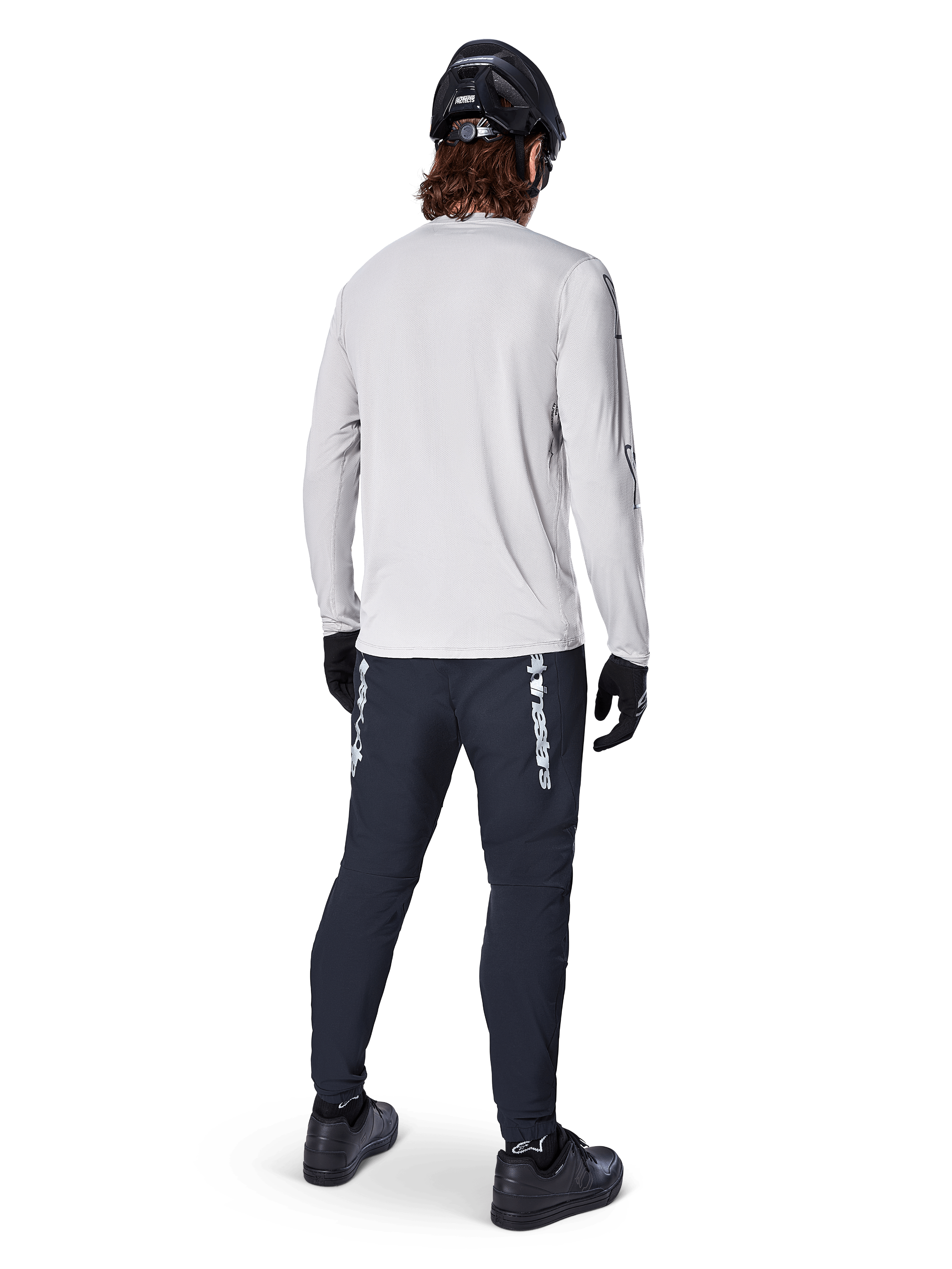 Camisola de Manga Longa Alpinestars A-Dura Switch, Cinzento Claro, vista traseira num ciclista a usar calças de ciclismo pretas, capacete e luvas, equipamento de BTT de alta performance com cauda mais longa.