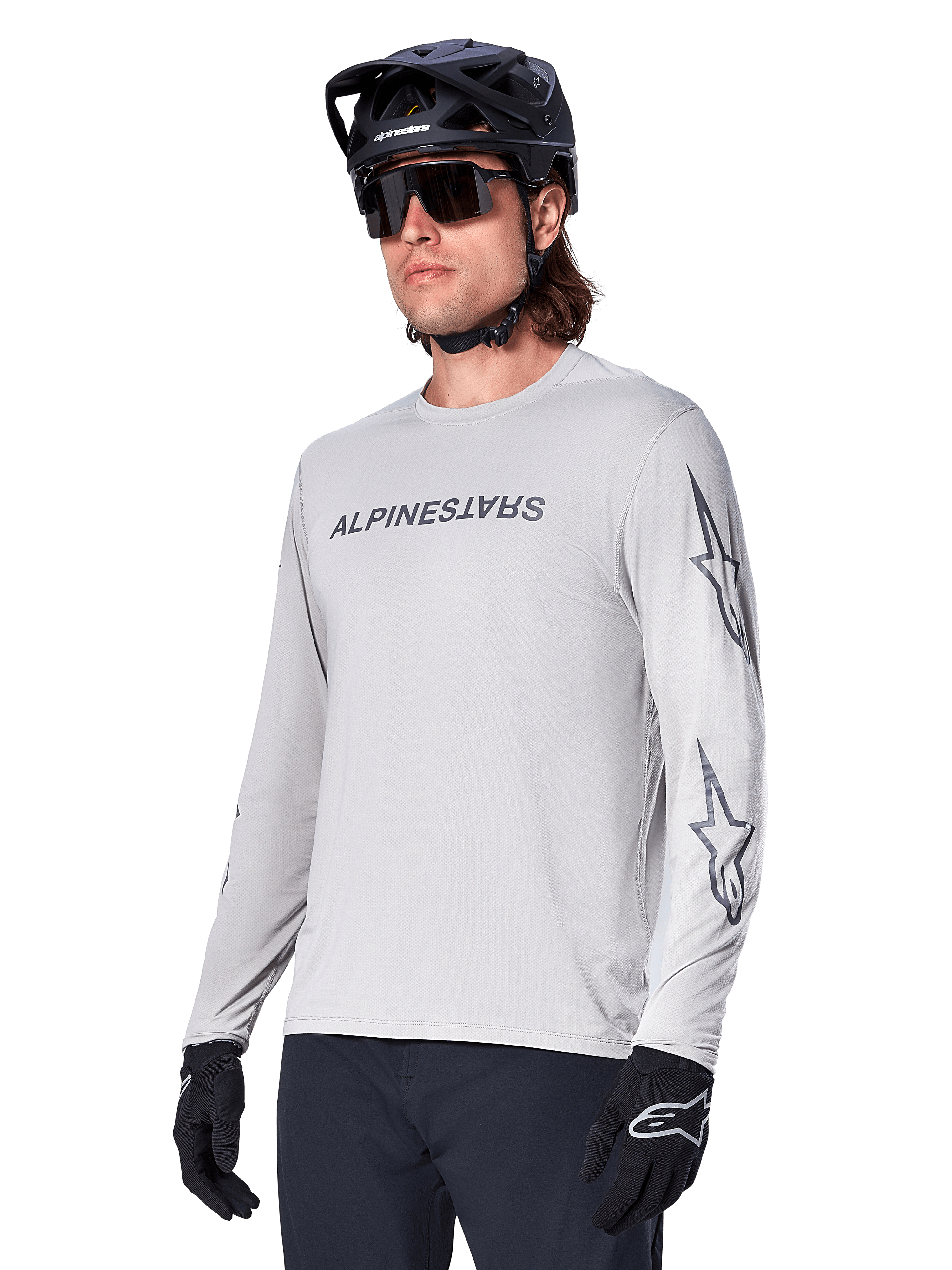 Alpinestars A-Dura Switch Long Sleeve Jersey, camisola de BTT, cinzento claro, logótipo nominativo em serigrafia preta no peito e logótipos de estrela nas mangas, usada com capacete de BTT preto, óculos de sol escuros e luvas pretas, equipamento atlético de ciclismo todo-o-terreno
