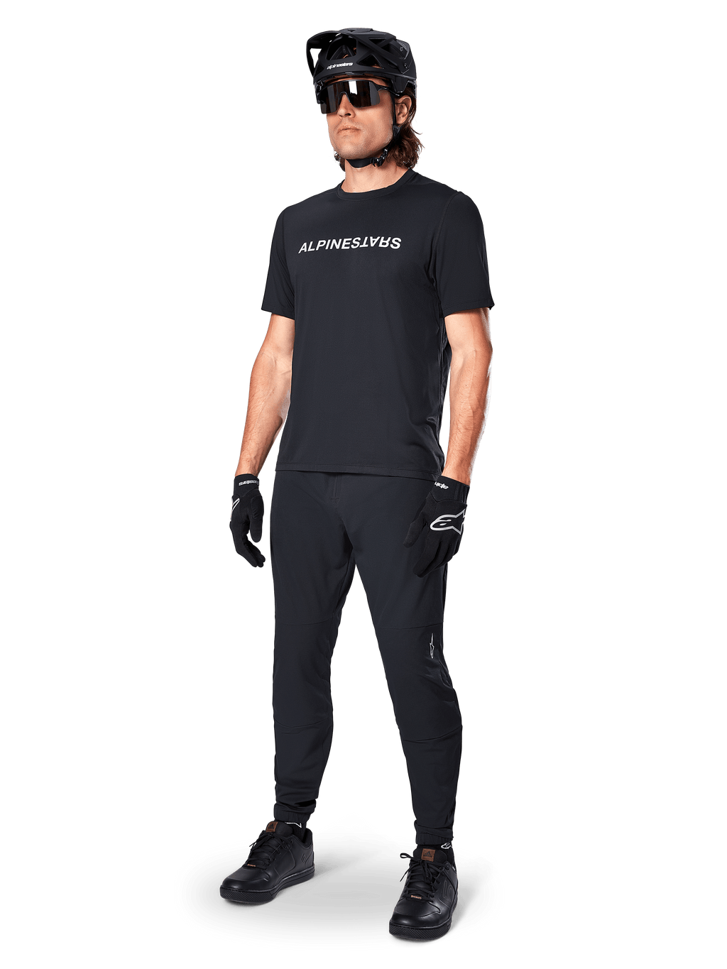 Camisola de Manga Curta Alpinestars A-Dura Switch, preta, vestida por um modelo com calças de BTT pretas a condizer, capacete e luvas, com o logótipo Alpinestars em branco no peito, vestuário de alta performance para ciclismo de montanha