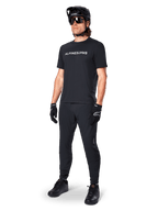 Camisola de Manga Curta Alpinestars A-Dura Switch, preta, vestida por um modelo com calças de BTT pretas a condizer, capacete e luvas, com o logótipo Alpinestars em branco no peito, vestuário de alta performance para ciclismo de montanha