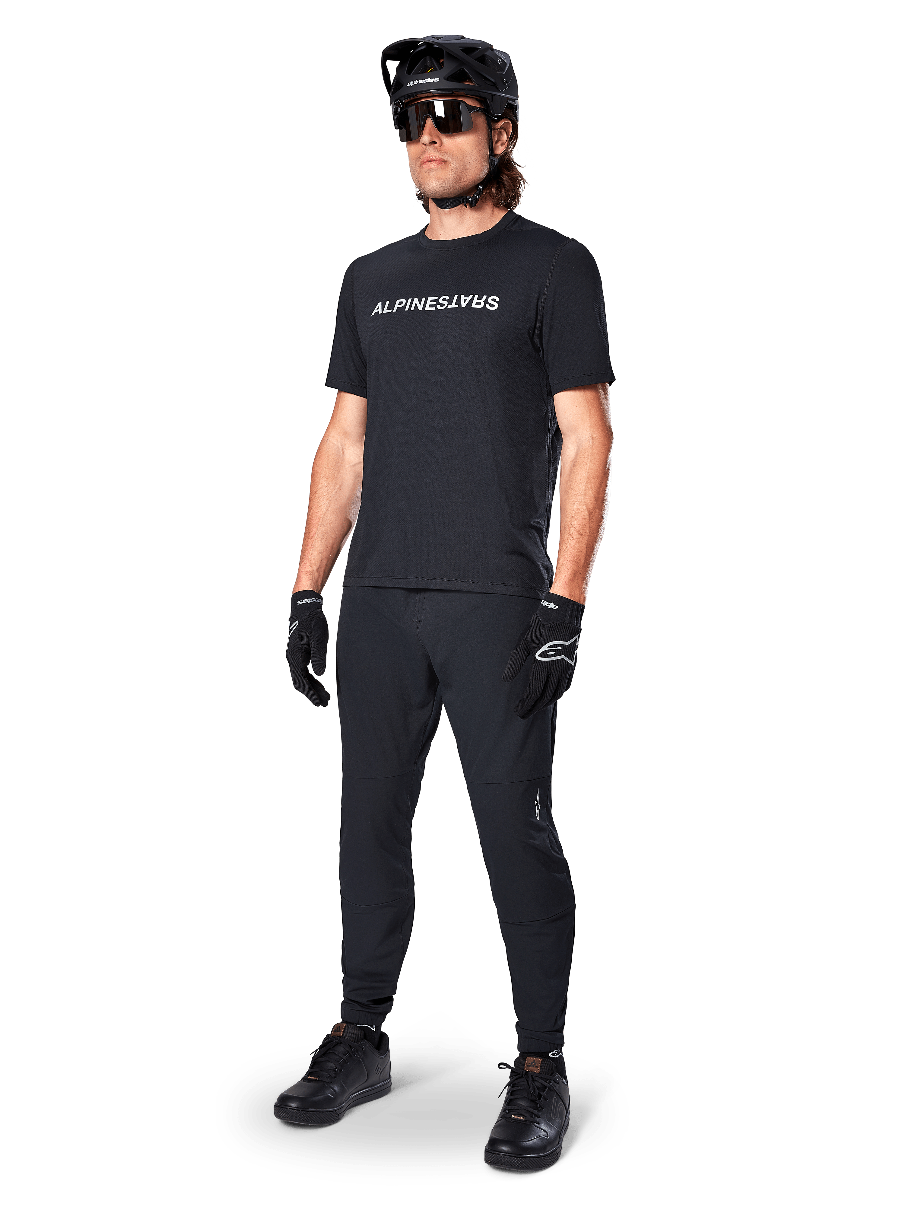 Camisola de Manga Curta Alpinestars A-Dura Switch, preta, vestida por um modelo com calças de BTT pretas a condizer, capacete e luvas, com o logótipo Alpinestars em branco no peito, vestuário de alta performance para ciclismo de montanha