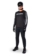 Alpinestars A-Dura Dri Oscar Long Sleeve Jersey, camisola de manga comprida, preto refletor, com logótipo Alpinestars branco no peito e padrões gráficos refletores nas mangas, usada com calças de BTT pretas, capacete e luvas, vestuário técnico de BTT