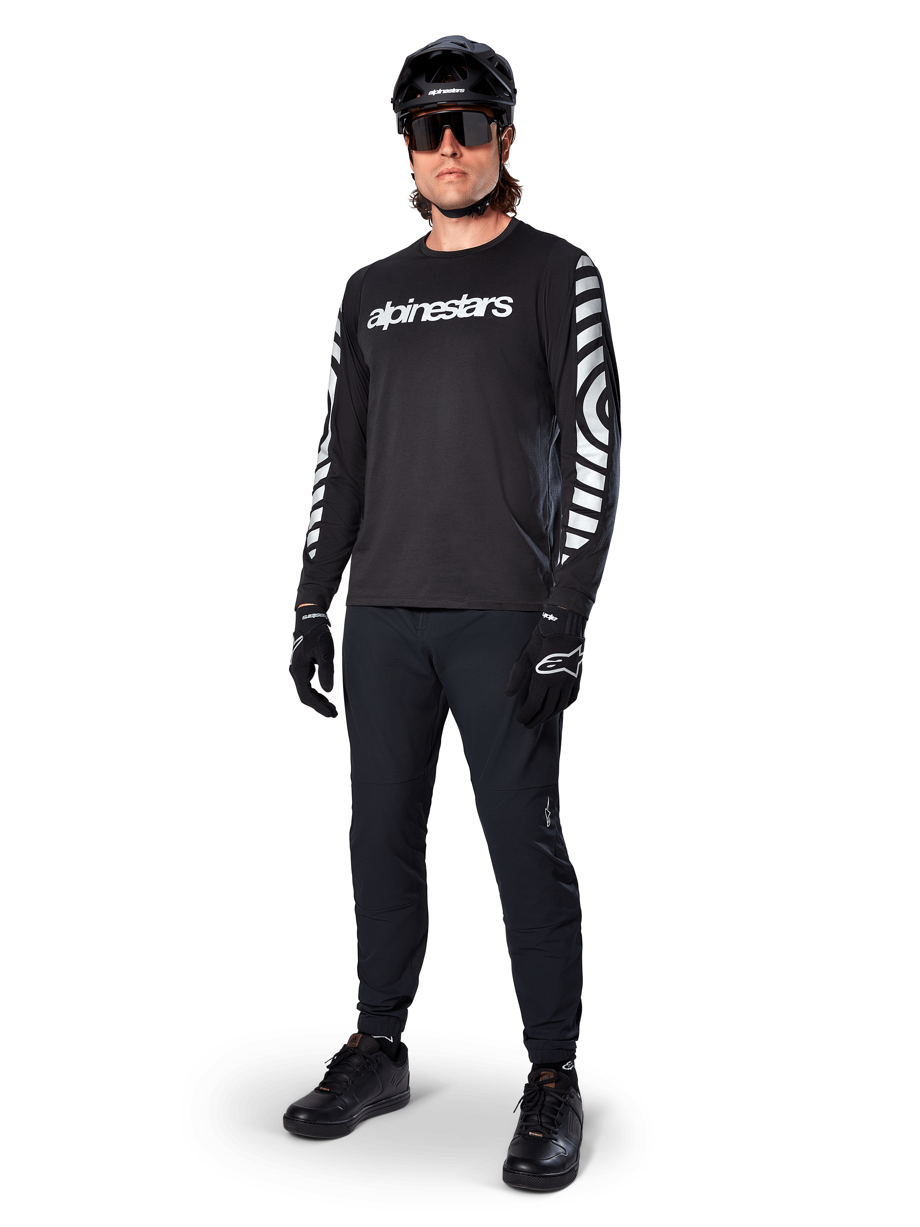 Alpinestars A-Dura Dri Oscar Long Sleeve Jersey, camisola de manga comprida, preto refletor, com logótipo Alpinestars branco no peito e padrões gráficos refletores nas mangas, usada com calças de BTT pretas, capacete e luvas, vestuário técnico de BTT