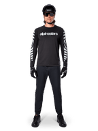 Alpinestars A-Dura Dri Oscar Long Sleeve Jersey em Black Reflective, usada com um capacete preto e óculos de sol, com logótipo branco no peito e padrões gráficos refletivos nas mangas, equipamento de MTB para percursos fora de estrada