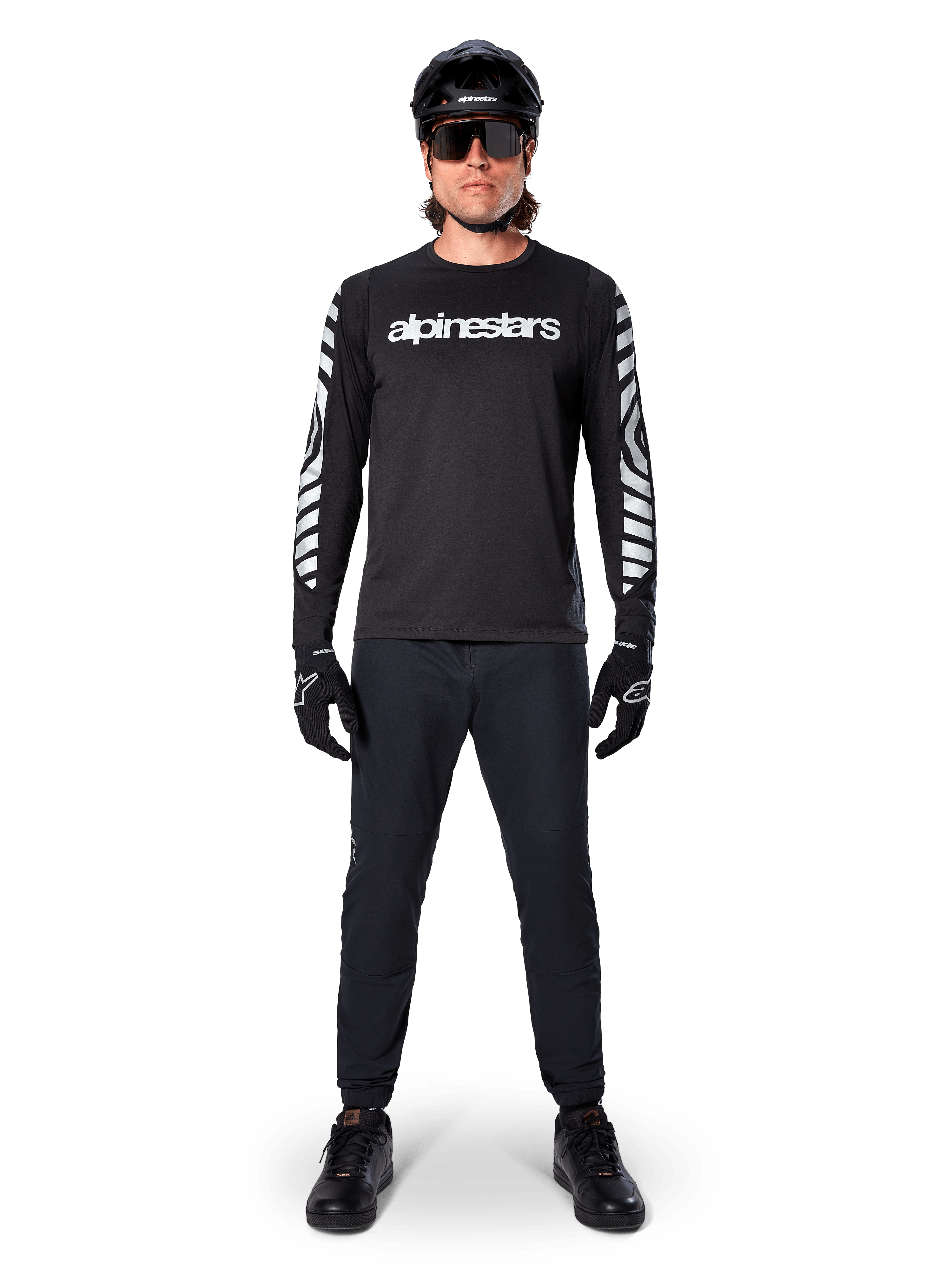 Alpinestars A-Dura Dri Oscar Long Sleeve Jersey em Black Reflective, usada com um capacete preto e óculos de sol, com logótipo branco no peito e padrões gráficos refletivos nas mangas, equipamento de MTB para percursos fora de estrada