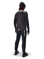 Ciclista de BTT com a camisola de manga comprida Alpinestars A-Dura Dri Oscar em Preto Refletor, vista de costas, calças técnicas pretas, capacete e luvas, com riscas refletoras nos ombros e cauda mais longa para ciclismo todo-o-terreno.