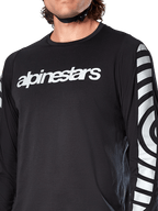 Camisola de Manga Comprida Alpinestars A-Dura Dri Oscar, Preto Refletor, vista em pormenor mostrando o logótipo Alpinestars branco no peito e gráficos circulares refletores nas mangas, vestuário técnico de ciclismo para BTT