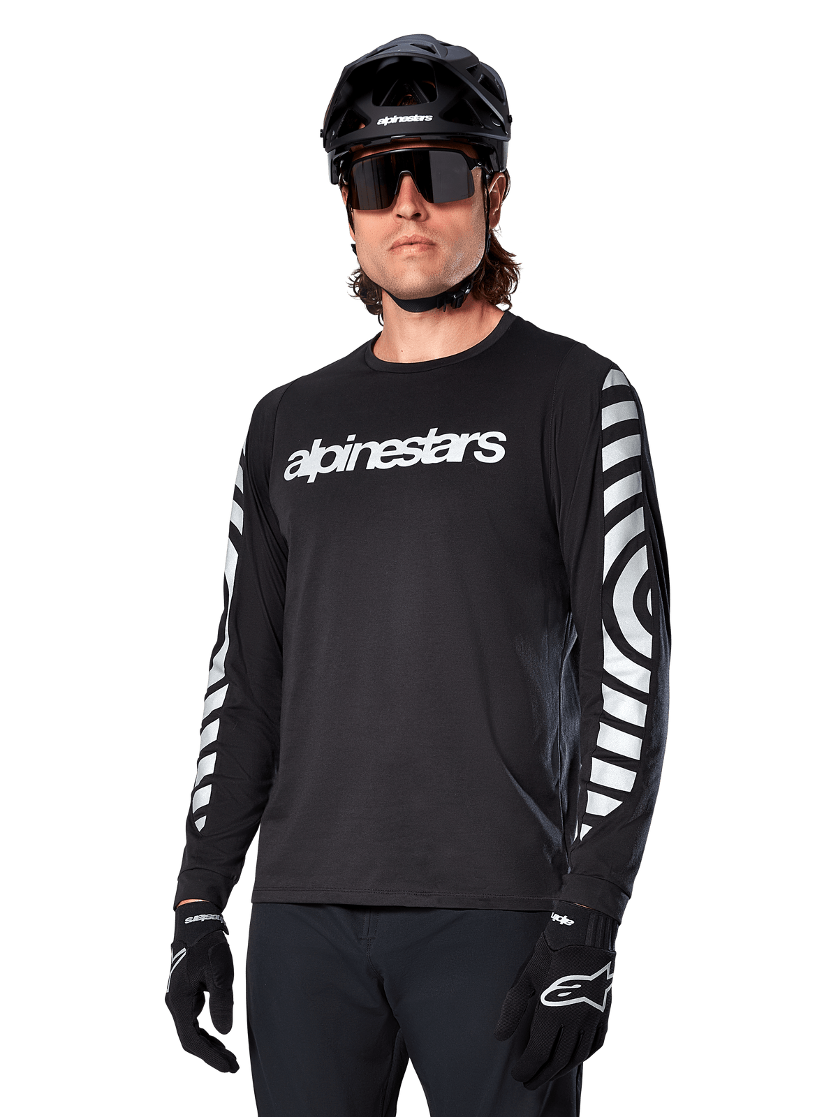 Camisola de manga comprida Alpinestars A-Dura Dri Oscar, camisola de ciclismo MTB, preto refletor, com logótipo branco no peito e gráficos circulares refletivos arrojados nas mangas, utilizada com um capacete preto e óculos de sol, vestuário técnico com gestão de humidade para ciclismo de montanha fora de estrada
