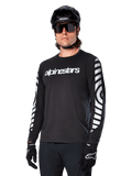 Camisola de manga comprida Alpinestars A-Dura Dri Oscar, camisola de ciclismo MTB, preto refletor, com logótipo branco no peito e gráficos circulares refletivos arrojados nas mangas, utilizada com um capacete preto e óculos de sol, vestuário técnico com gestão de humidade para ciclismo de montanha fora de estrada