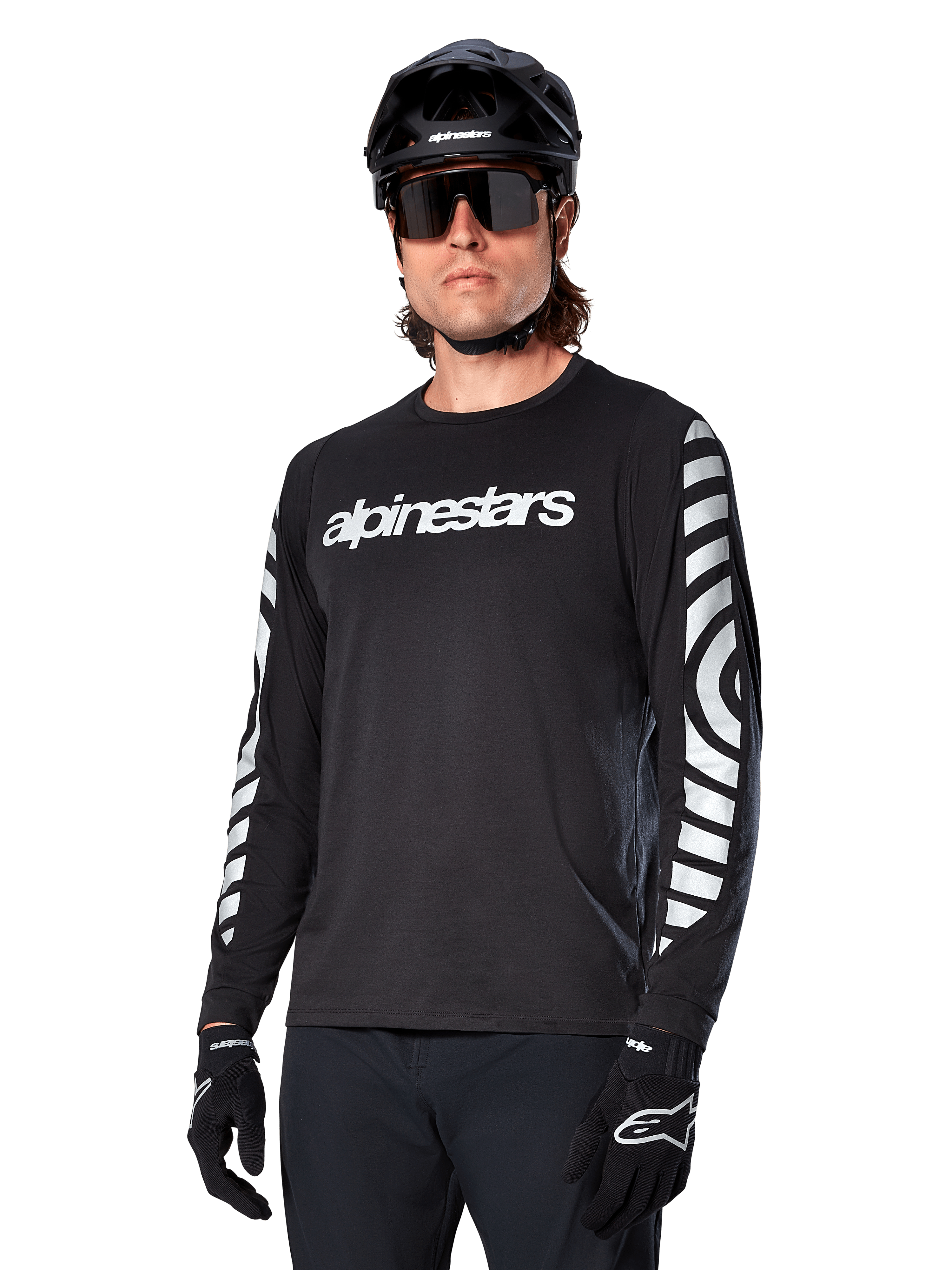 Camisola de manga comprida Alpinestars A-Dura Dri Oscar, camisola de ciclismo MTB, preto refletor, com logótipo branco no peito e gráficos circulares refletivos arrojados nas mangas, utilizada com um capacete preto e óculos de sol, vestuário técnico com gestão de humidade para ciclismo de montanha fora de estrada