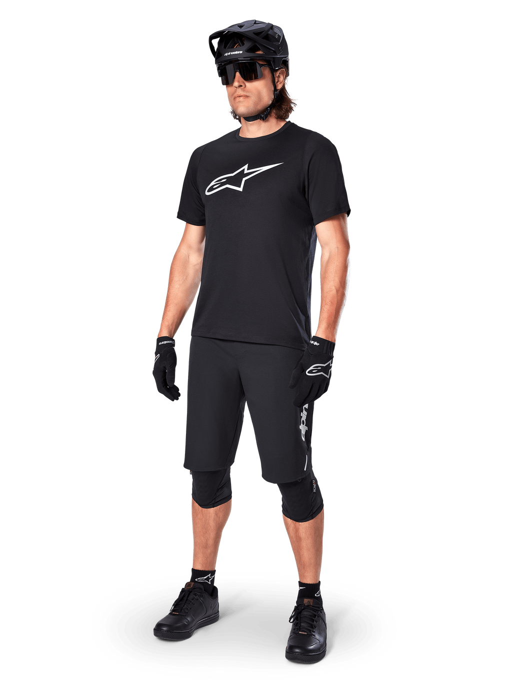 Ciclista de BTT a usar a camisola de manga curta Alpinestars A-Dura Dri Oscar em preto refletor, com um logótipo branco de grandes dimensões no peito, combinada com calções de BTT pretos, luvas e capacete, vestuário técnico de ciclismo para performance fora de estrada