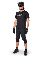Ciclista de BTT a usar a camisola de manga curta Alpinestars A-Dura Dri Oscar em preto refletor, com um logótipo branco de grandes dimensões no peito, combinada com calções de BTT pretos, luvas e capacete, vestuário técnico de ciclismo para performance fora de estrada
