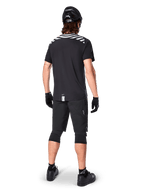 Alpinestars A-Dura Dri Oscar Short Sleeve Jersey, Preto Refletor, vista traseira de um ciclista a usar a camisola com calções de BTT pretos, capacete e joelheiras, com grafismos refletores nos ombros e design de cauda longa para a prática de BTT.