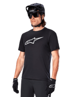 Alpinestars A-Dura Dri Oscar Jersey, camisola de ciclismo BTT de manga curta, preta com logótipo branco, tecido técnico de alto desempenho com gestão de humidade, usada com capacete preto, óculos de sol e luvas