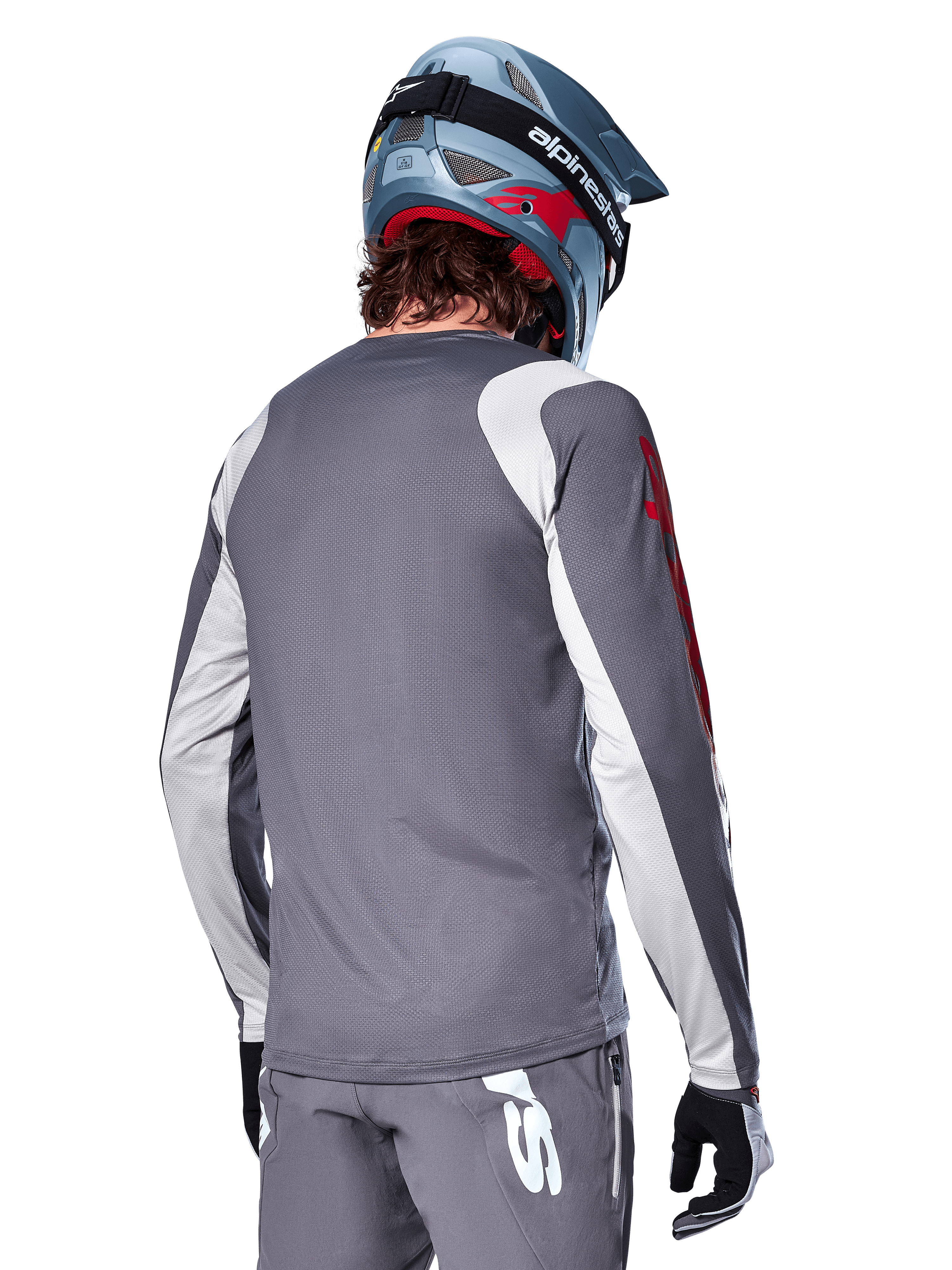 Camisola de Manga Comprida Alpinestars A-Supra Astar, cinzento escuro com painéis cinzento claro nos ombros e braços, vista traseira de ciclista com capacete integral de mountain bike azul e calças cinzentas, vestuário de ciclismo MTB de ajuste de performance