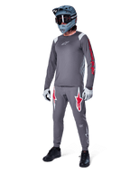 Camisola de Manga Comprida Alpinestars A-Supra Astar em cinzento escuro, com branding vermelho nas mangas e logótipo branco no peito, usada por um ciclista com calças cinzentas a condizer, capacete integral cinza-azulado e luvas de performance, equipamento coordenado de BTT para gravity