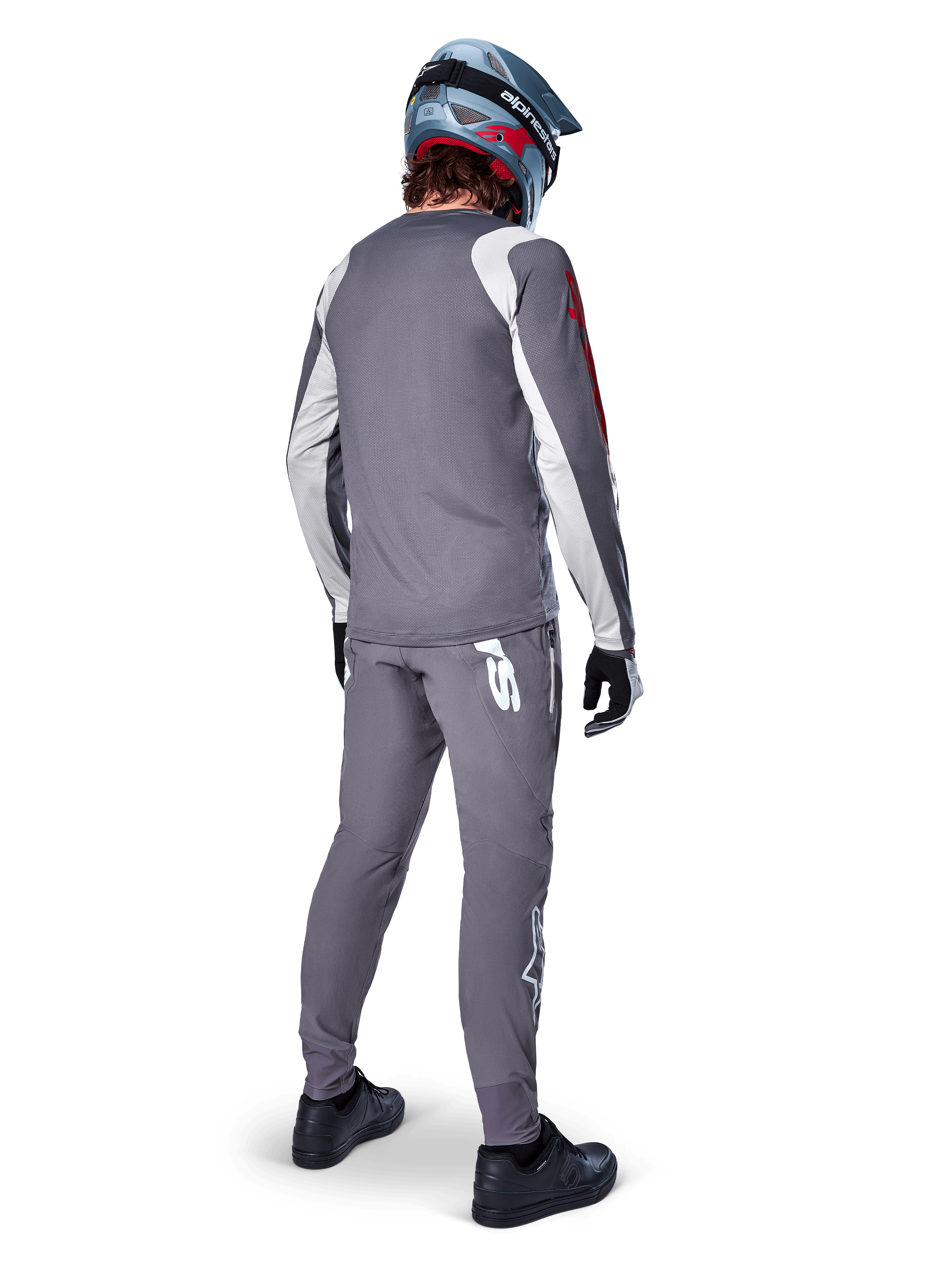 Camisola Alpinestars A-Supra Astar, camisola de BTT de manga comprida, cinzento escuro com detalhes brancos nas mangas e logótipo vermelho, vista traseira de ciclista a usar calças cinzentas a condizer e capacete integral azul, vestuário de ciclismo de performance