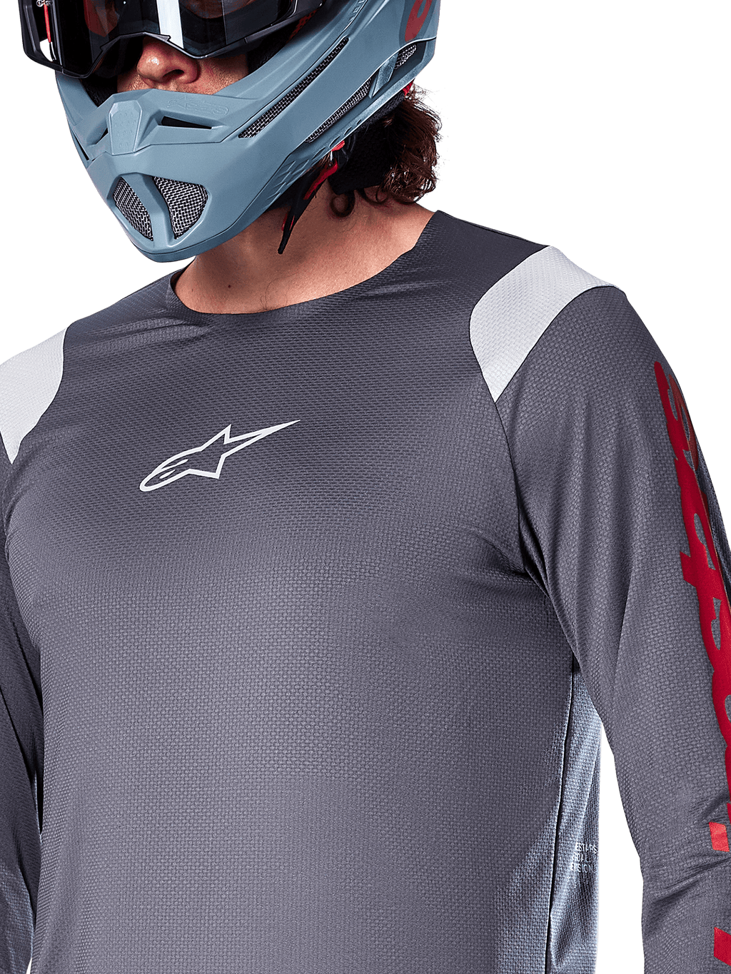 Camisola de Manga Comprida Alpinestars A-Supra Astar, cinza escuro com painéis brancos nos ombros e grafismos vermelhos na manga, usada com um capacete integral cinza-azulado claro, vestuário de BTT de alta performance