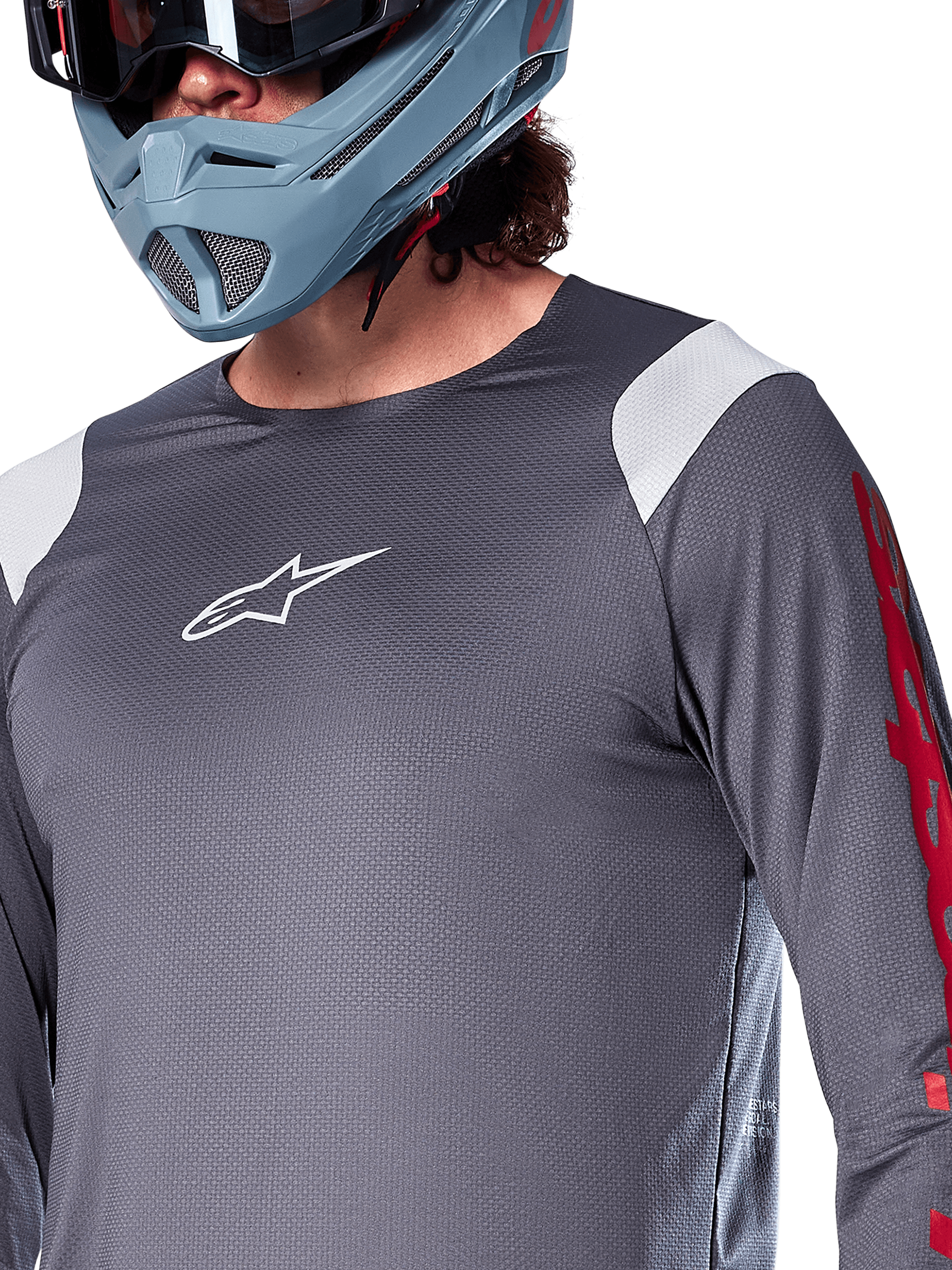 Camisola de Manga Comprida Alpinestars A-Supra Astar, cinza escuro com painéis brancos nos ombros e grafismos vermelhos na manga, usada com um capacete integral cinza-azulado claro, vestuário de BTT de alta performance