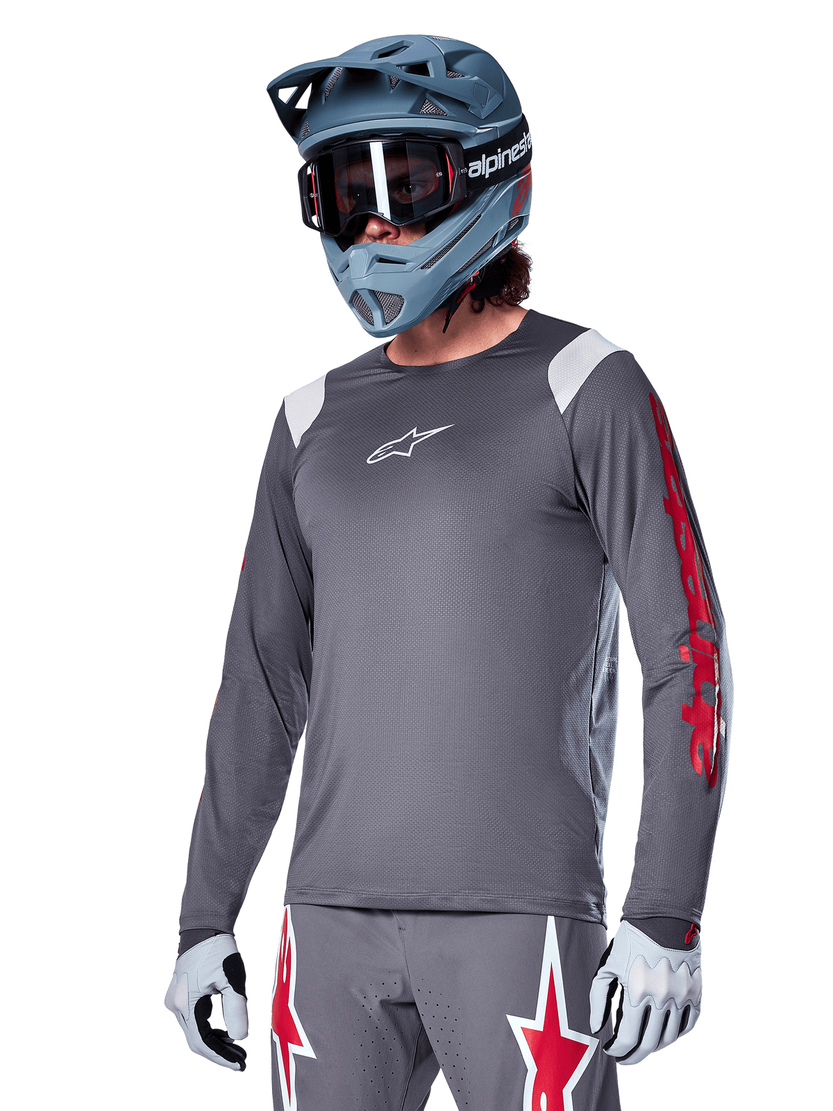 Alpinestars A-Supra Astar Jersey de manga comprida, jersey de BTT, cinzento escuro com detalhes em vermelho e branco, ajuste de performance, usado com calças cinzentas a condizer com gráficos de estrelas vermelhas e brancas, equipamento completo de ciclismo off-road com capacete integral e luvas