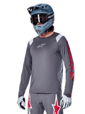 Alpinestars A-Supra Astar Jersey de manga comprida, jersey de BTT, cinzento escuro com detalhes em vermelho e branco, ajuste de performance, usado com calças cinzentas a condizer com gráficos de estrelas vermelhas e brancas, equipamento completo de ciclismo off-road com capacete integral e luvas