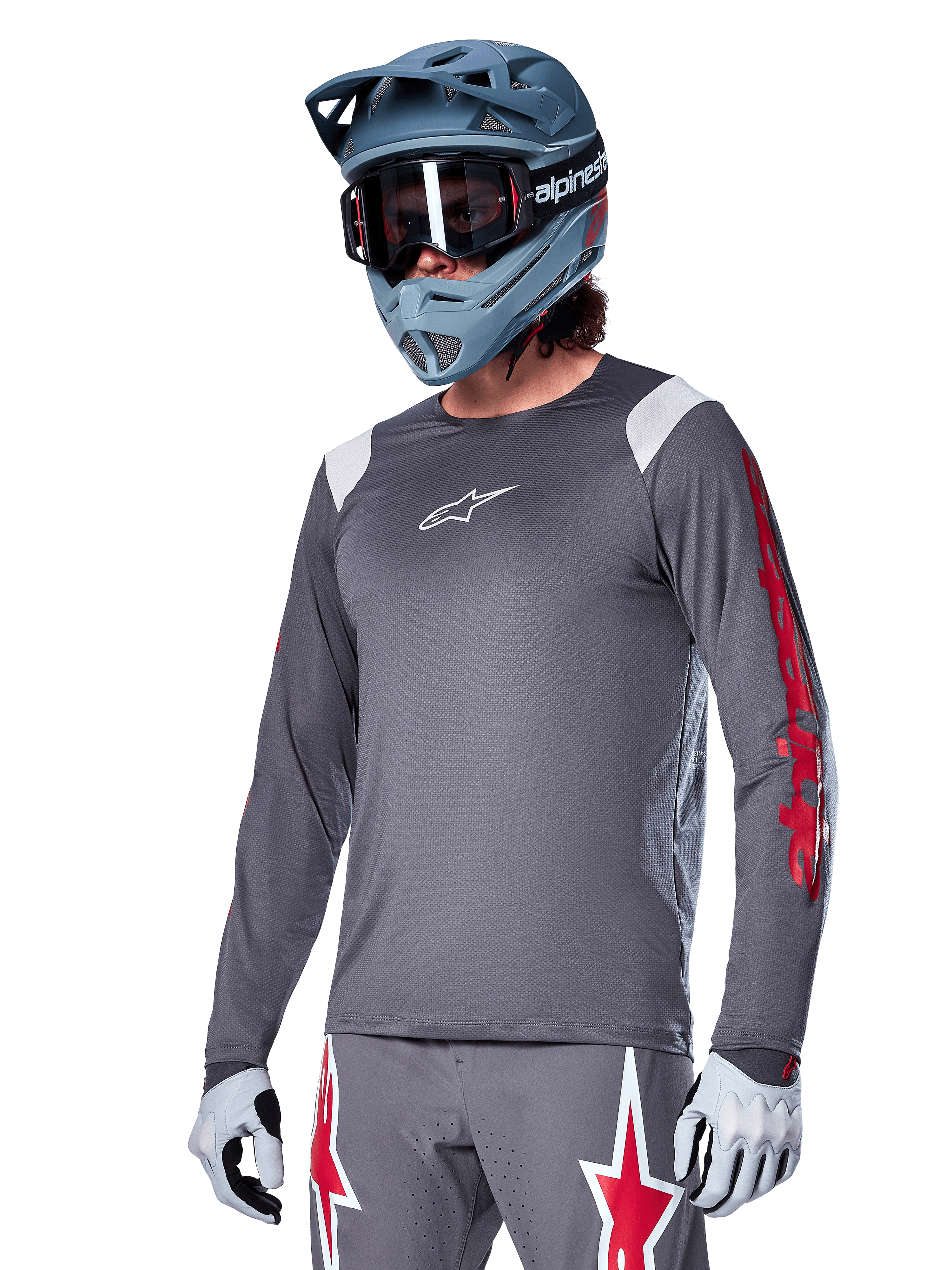 Alpinestars A-Supra Astar Jersey de manga comprida, jersey de BTT, cinzento escuro com detalhes em vermelho e branco, ajuste de performance, usado com calças cinzentas a condizer com gráficos de estrelas vermelhas e brancas, equipamento completo de ciclismo off-road com capacete integral e luvas