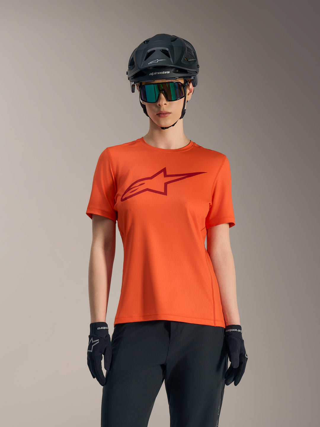 Stella A-Dura Ride Jersey laranja de manga curta para mulher, logótipo vermelho, capacete de BTT preto e óculos de sol.