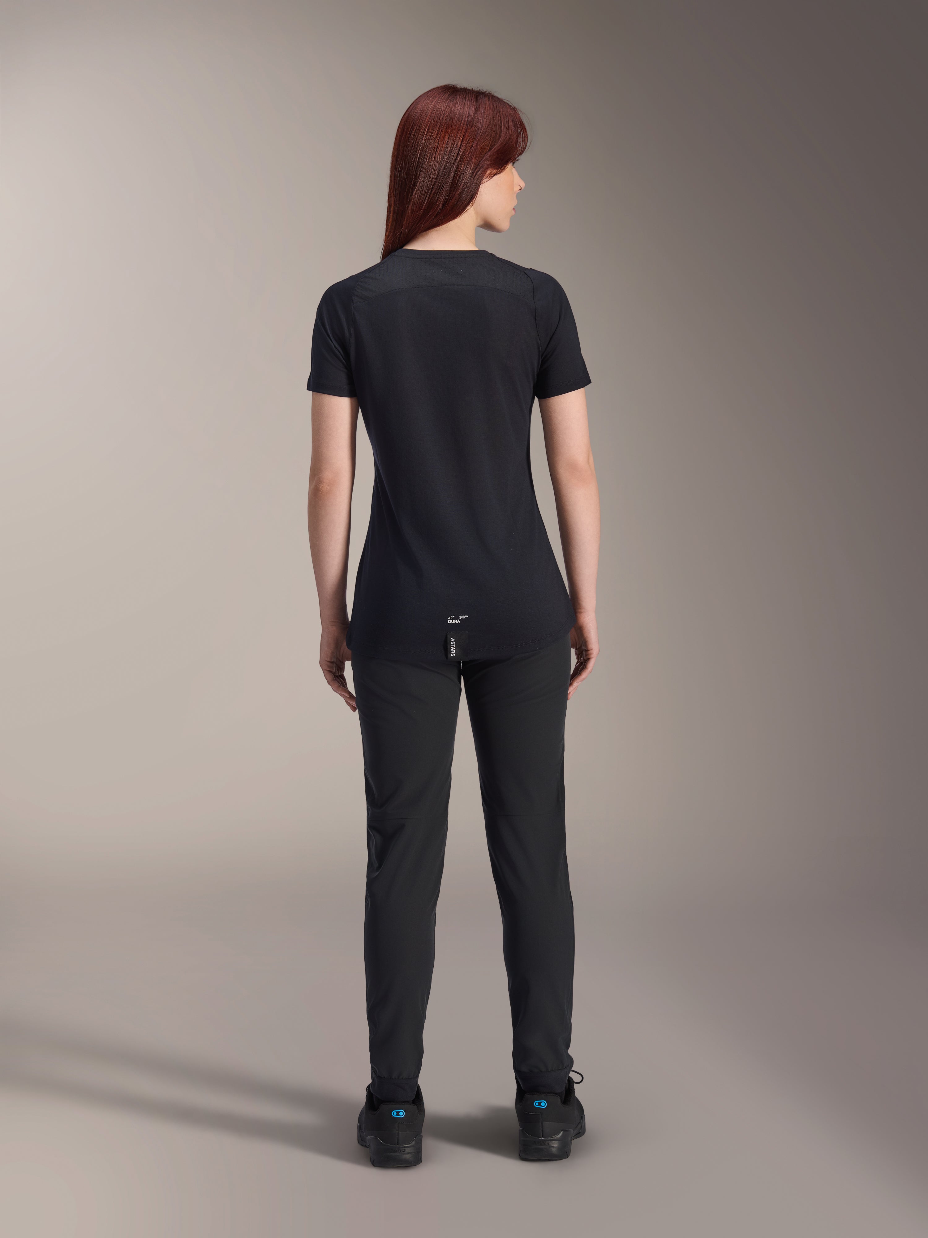 Alpinestars Women Stella A-Dura Dri Switch Short Sleeve Jersey, Black, rear view on a model, featuring a longer drop tail and technical mesh panels, paired with black pants, performance MTB cycling gear